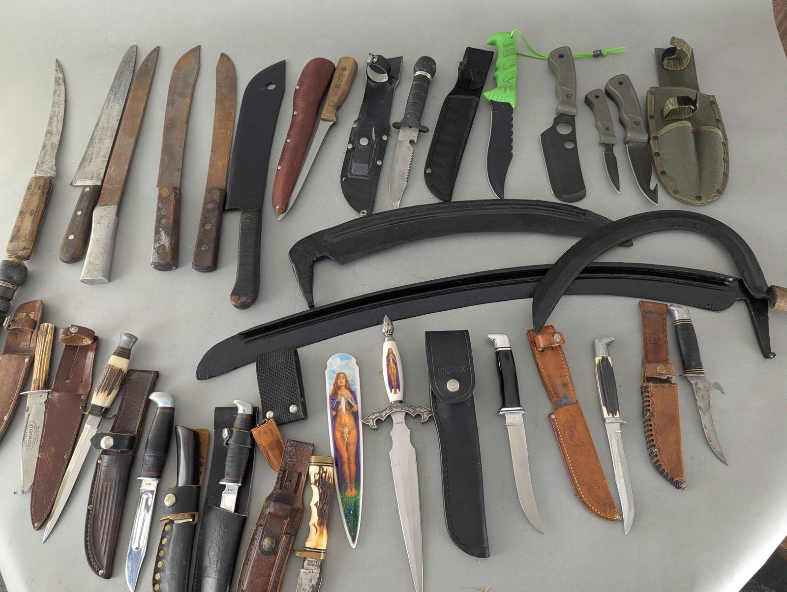 Collection of Knives with Sheaths and Assorted Blades: Assorted collection of knives, swords, and blades, featuring various designs and materials. Collection includes fixed-blade knives, machetes, and decorative daggers. Several pieces feature leather or