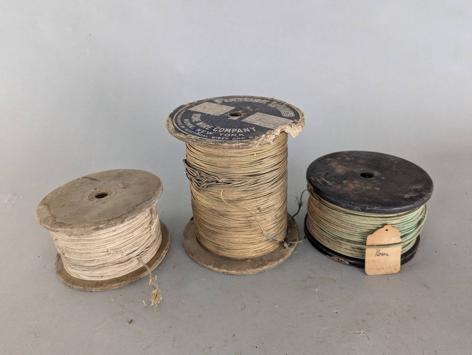 Antique Spools of Cloth Covered Wire by Rome Wire Company: Three antique spools of cloth covered wire, including one marked by the Rome Wire Company. The spools vary in size and appearance. The Rome Wire Company spool features a partially intact label with ma