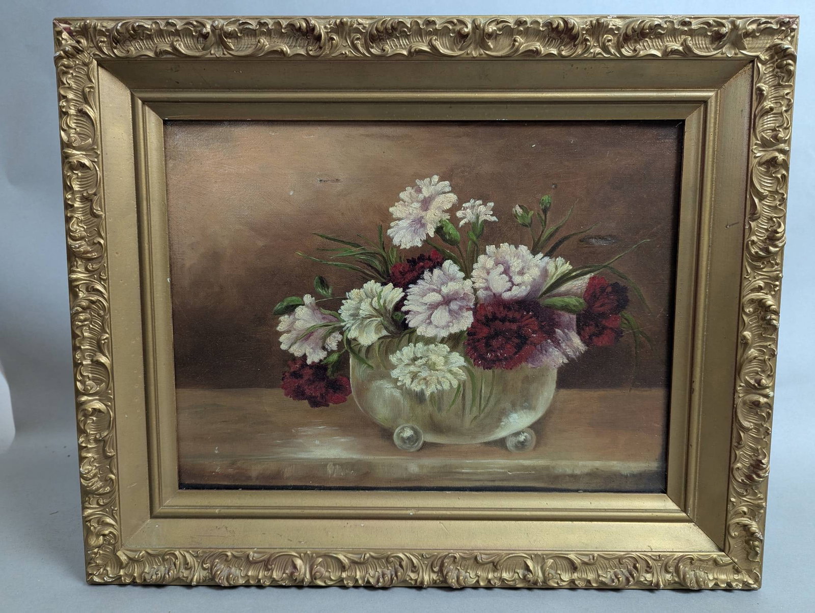 Floral Oil Painting in Gilded Frame with Glass Bowl Design: Oil painting featuring a floral arrangement of predominantly white and red flowers set in a clear glass bowl with ball-like supports. Framed in an ornate gilded frame, the artwork measures 21 inches i