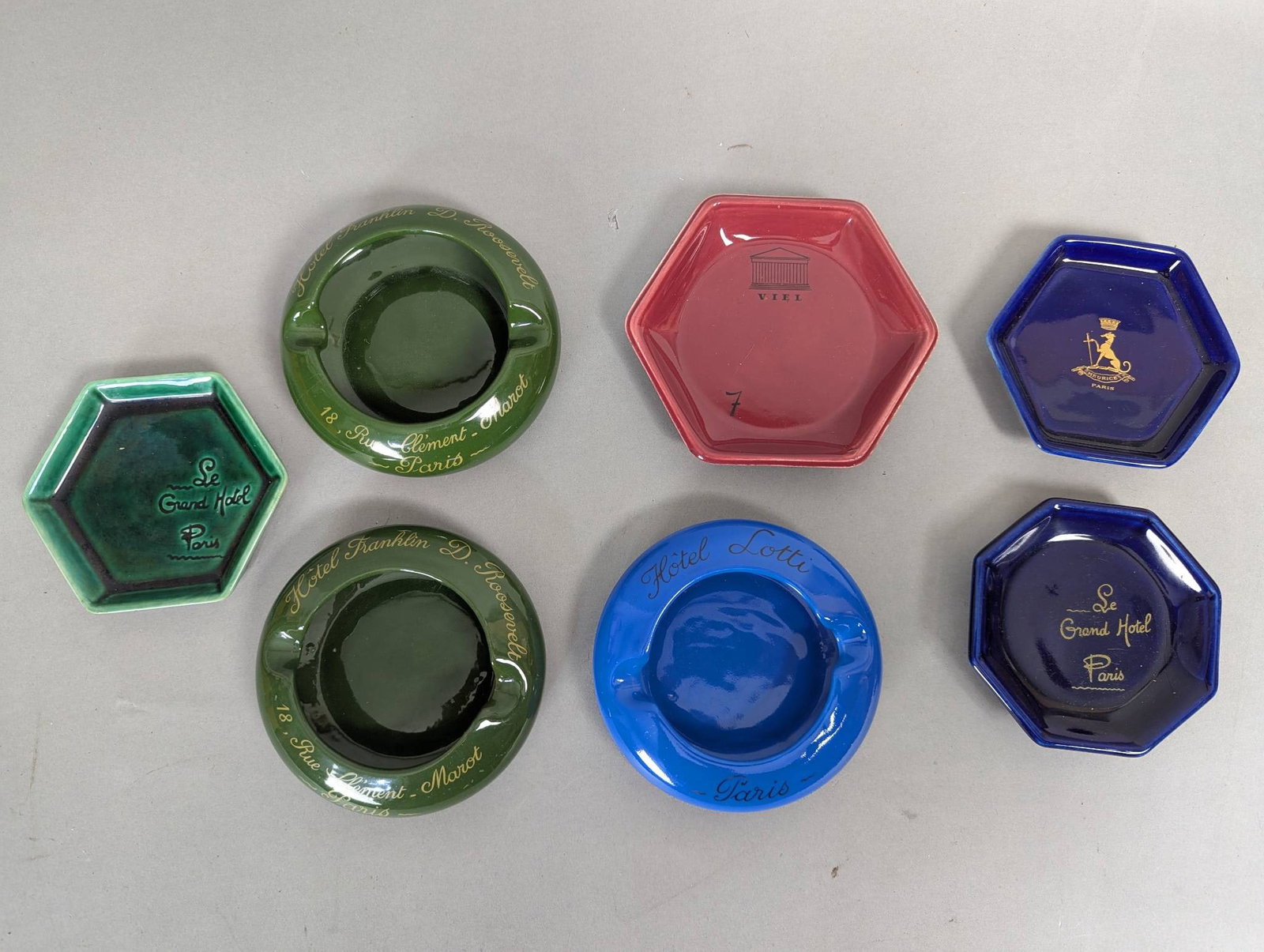 Lot of 7 Paris Hotel Ashtrays Made by St Uze Drome: Paris hotel ashtrays, made by St Uze Drome. The largest ashtray measures approximately 5 inches in height, 5 inches in width, and 1 inch in depth. The set includes seven ashtrays, each featuring uniqu