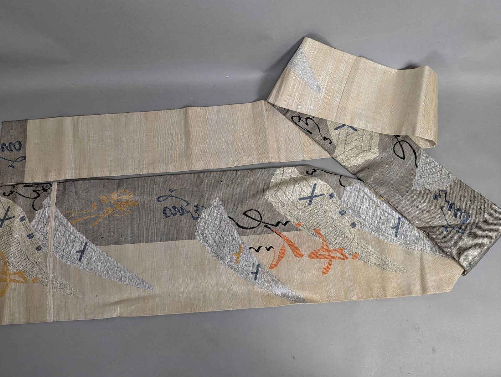 Japanese Vintage Silk Nagoya Obi Fabric: Japanese vintage Nagoya obi crafted from silk. Features a detailed abstract and traditional woven pattern with shades of silver, orange, and blue. The obi measures approximately 12 inches in height an