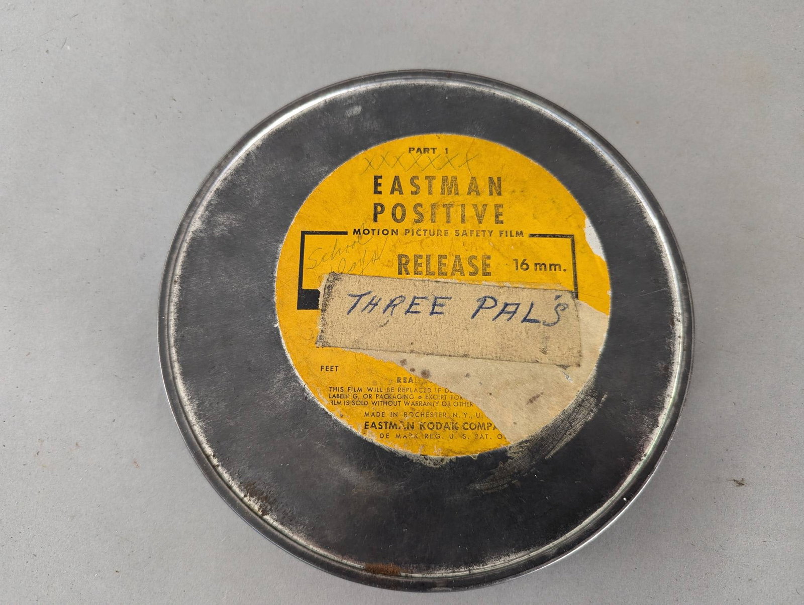 Grindhouse Era 16mm Film Reel Three Pals Eastman Positive: 16mm film reel titled Three Pals, housed in an Eastman Positive motion picture film canister. Includes clear labeling on the canister and features black-and-white frames visible on the reel, typical o