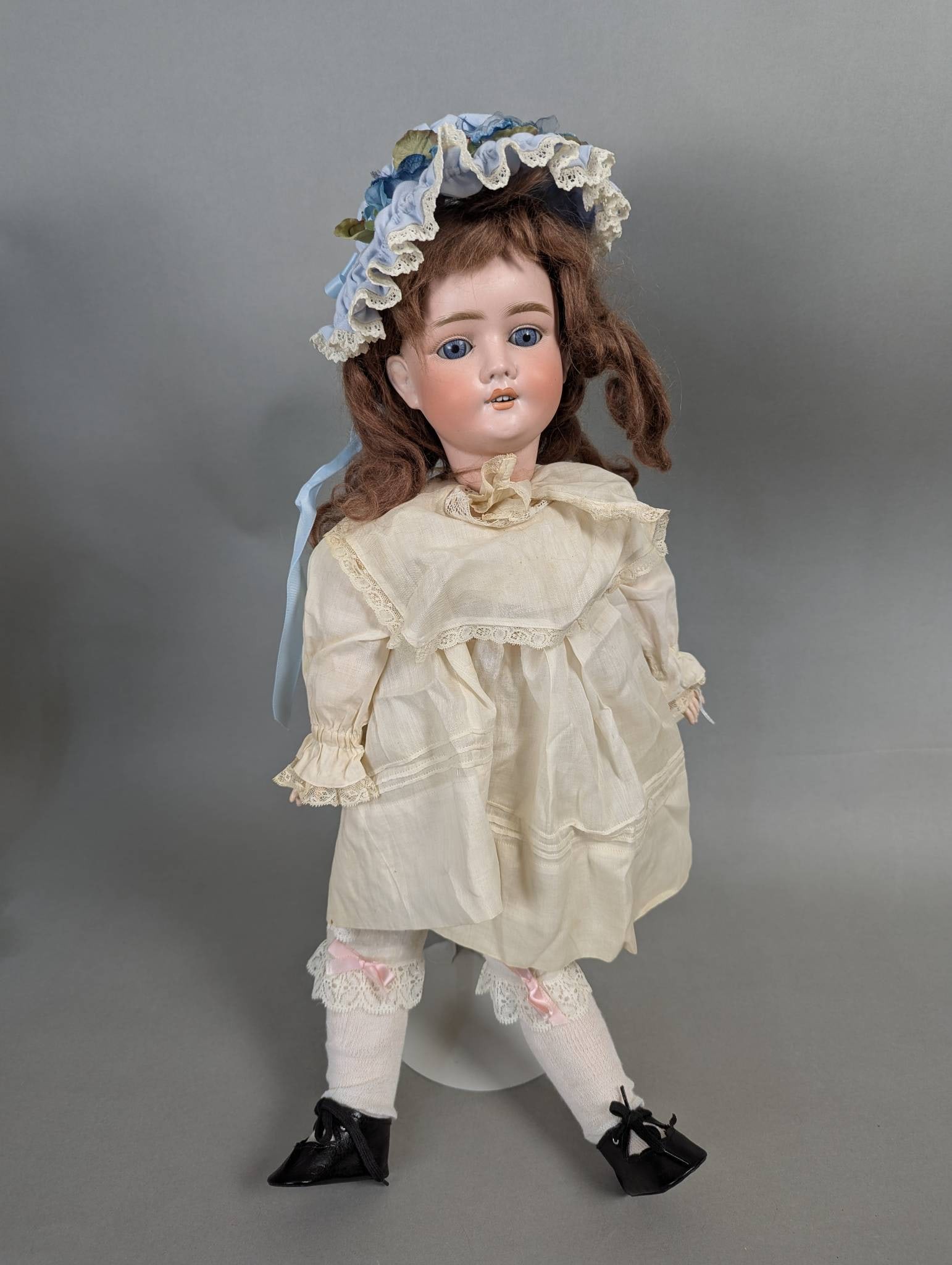 Kley and Hahn Bisque Head Doll with Original Dress: Kley and Hahn bisque head doll, measuring 24 inches in height, 9 inches in width, and 5 inches in depth. The doll features blue glass eyes, molded and painted facial features, and a light brown wig ad
