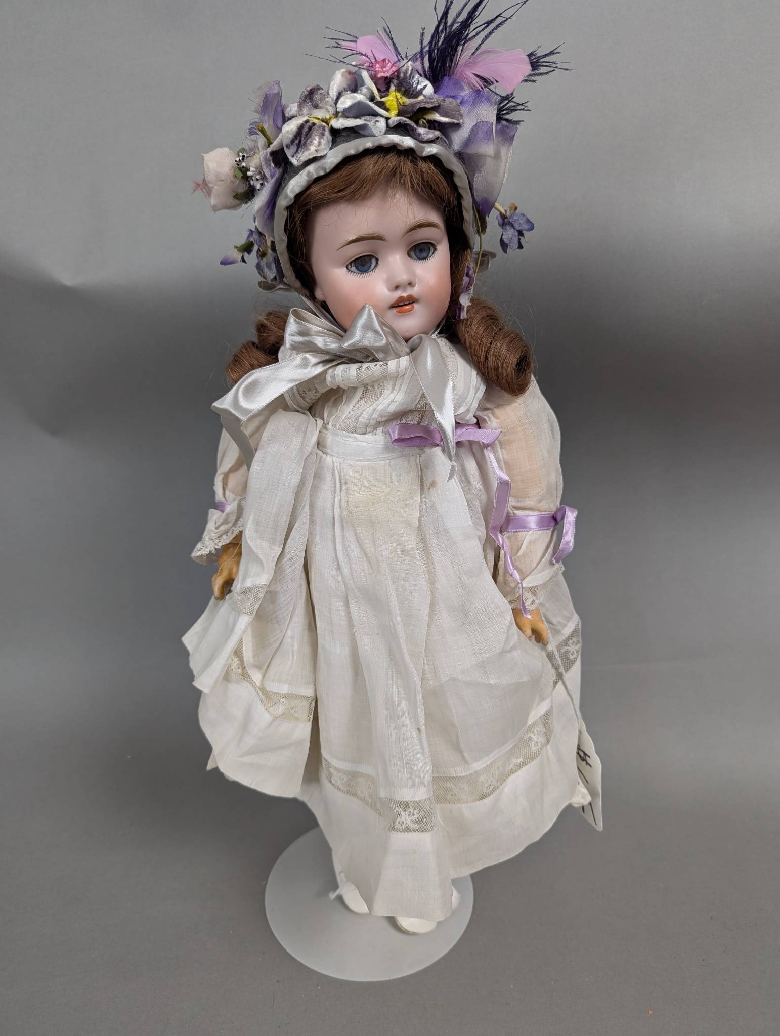 Porcelain Doll with Victorian-Style Outfit and Ribbon Accents: Porcelain doll measuring 19 inches in height, 9 inches in width, and 3 inches in depth. The doll features a bisque head with painted facial details, blue glass eyes, and brown synthetic hair styled in