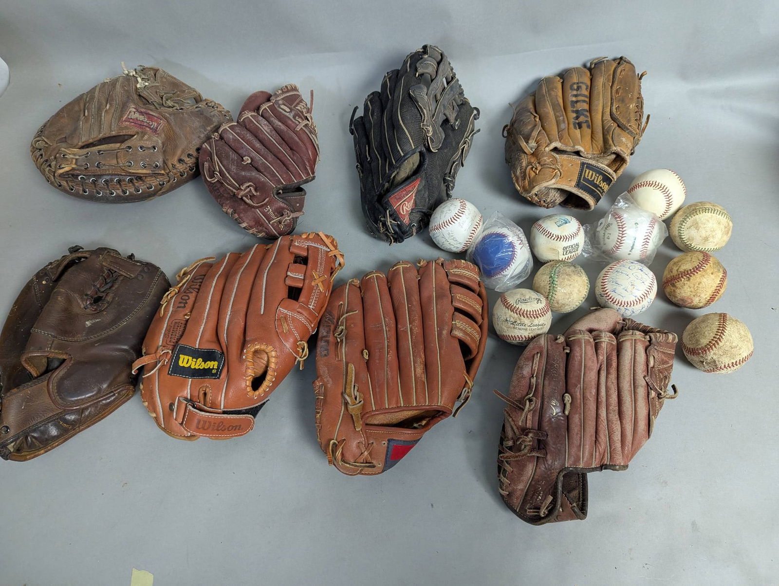 Baseball Gloves and Baseballs Including Wilson and Rawlings: An assortment of vintage and used baseball gloves and baseballs. Included in this collection are gloves from brands such as Wilson and Rawlings, with various designs, conditions, and leather finishes.