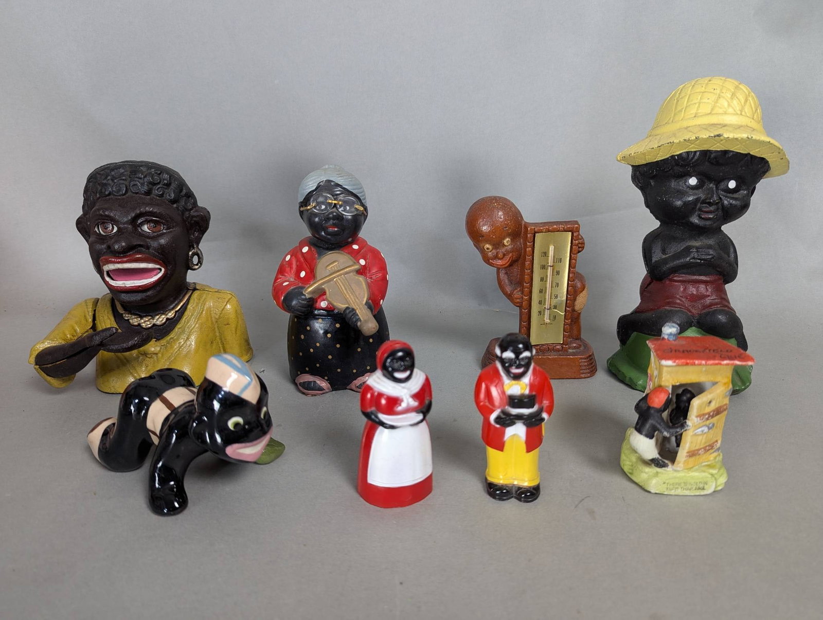 Black Memorabilia Including Banks and Figurines: Black memorabilia consisting of eight pieces, including coin banks, figurines, and a thermometer. Largest bank measures 9 inches high, 5 inches wide, and 4 inches deep. Items feature a variety of desi