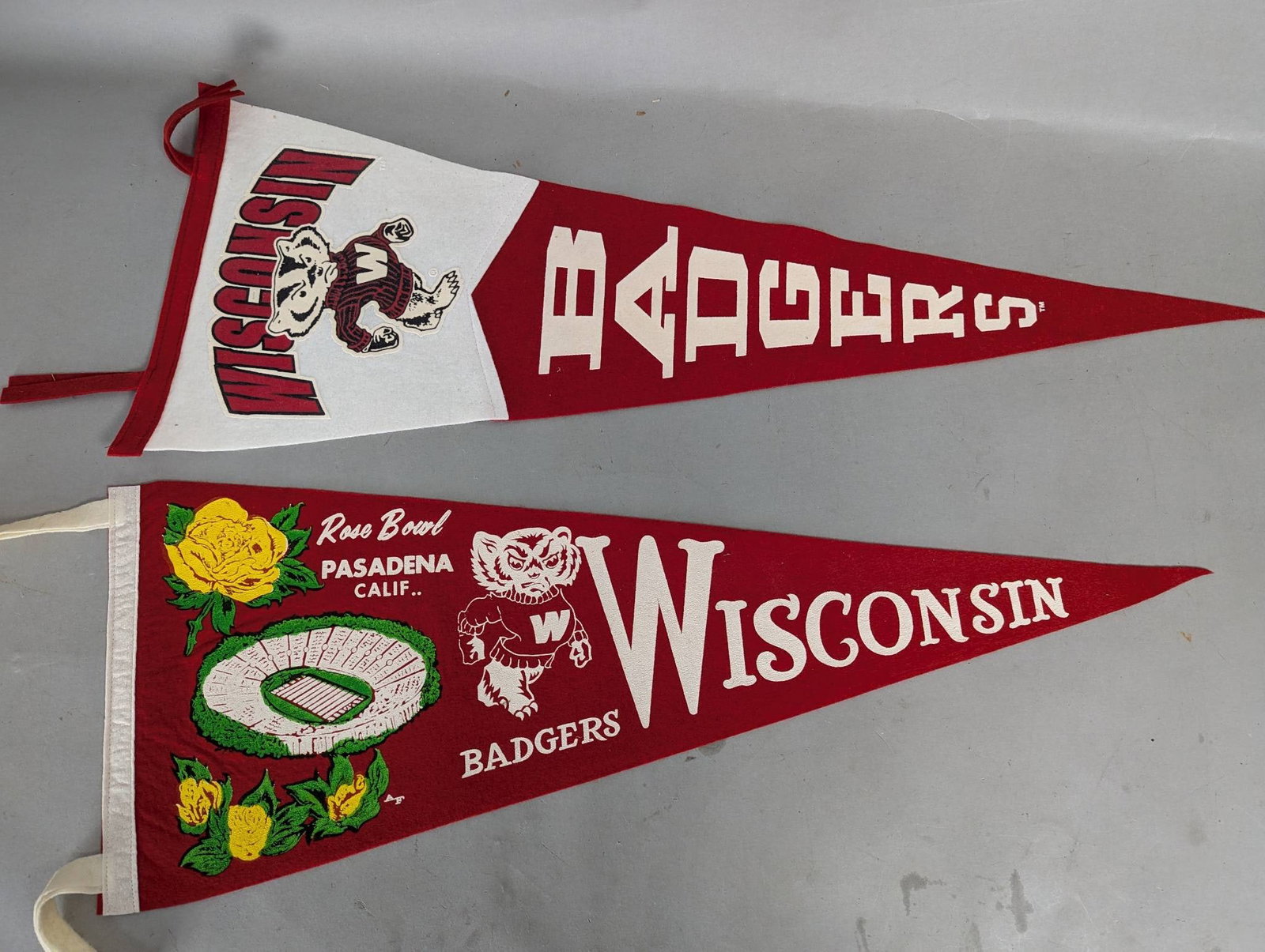 Wisconsin Badgers Pennants from 1963 Rose Bowl: Wisconsin Badgers felt pennants commemorating the 1963 Rose Bowl. The first pennant predominantly features the Badgers mascot Bucky Badger, with bold red and white graphics. The second pennant, also i