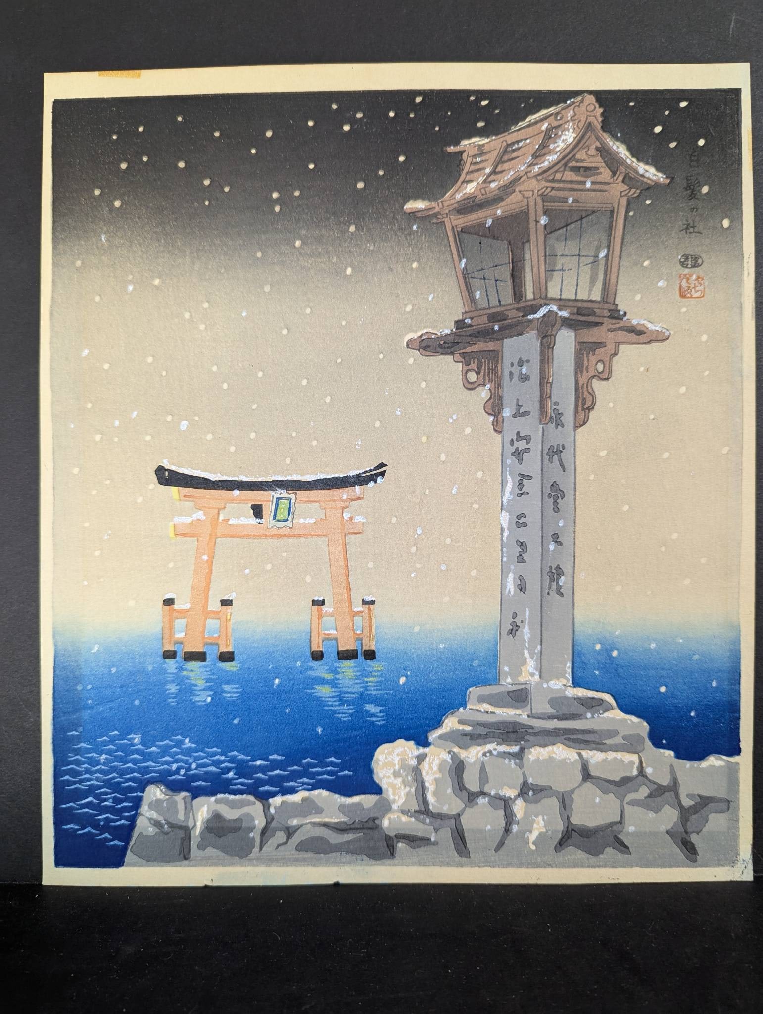 Tomikichiro Tokuriki Woodblock Print Depicting Shrine with Lantern and Torii Gate: Japanese woodblock print by Tomikichiro Tokuriki, depicting a serene shrine scene with a prominent lantern and torii gate against a snowy evening sky. The artist, Tomikichiro Tokuriki (1902-1999), was