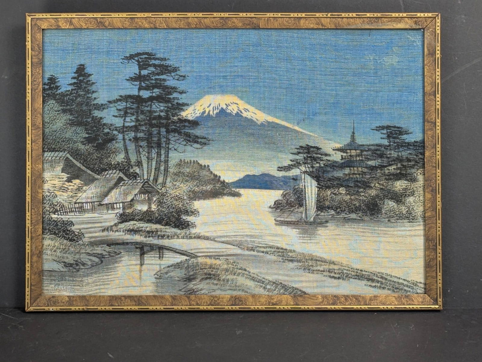 Painting on Silk Depicting Mount Fuji and Rural Scenery, c1930s: This painting on silk depicts a serene rural landscape with Mount Fuji in the backdrop, accompanied by traditional Japanese architectural elements, trees, and a sailboat on a calm river. The art dates
