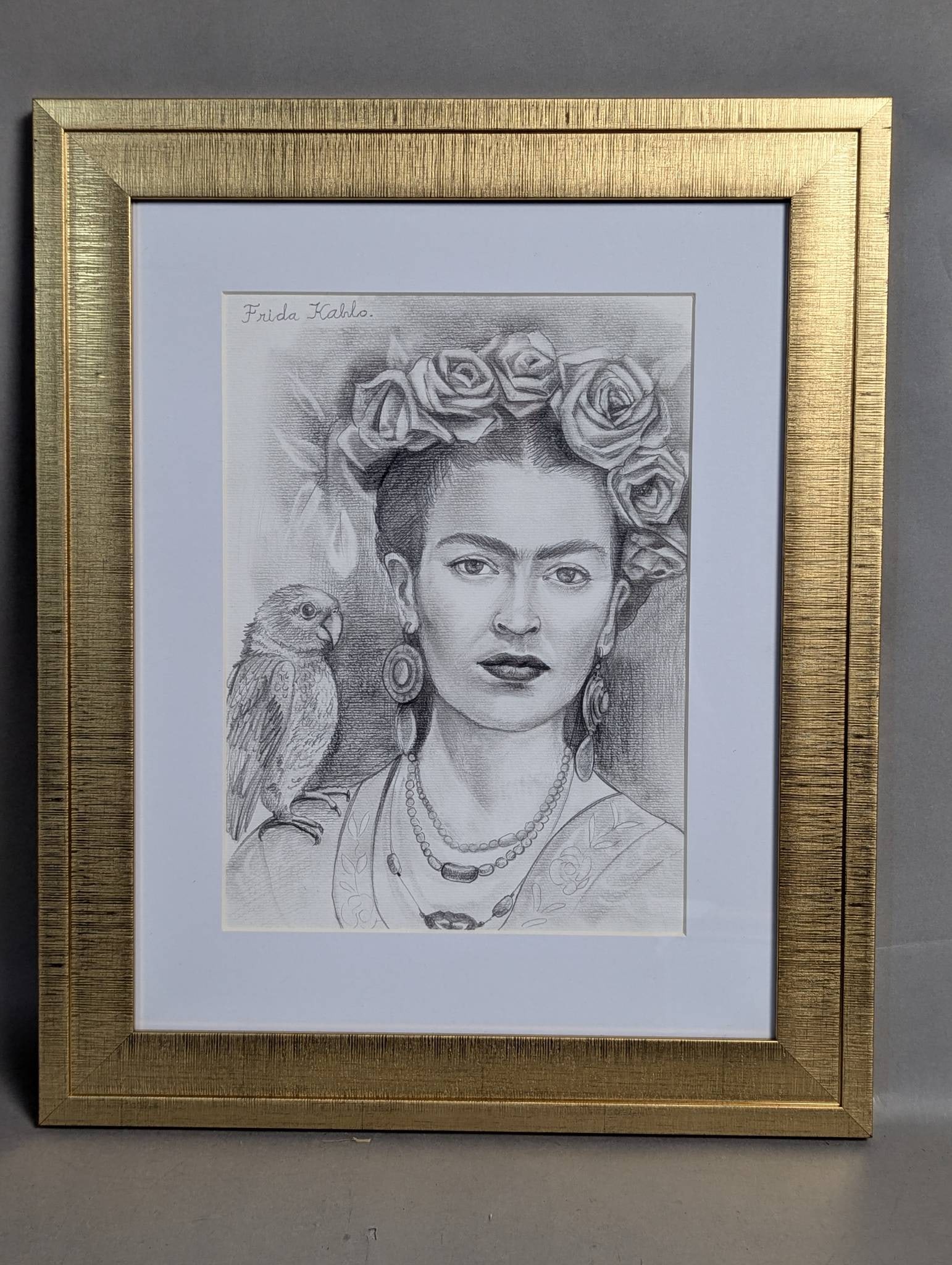 Framed Portrait Drawing Depicting Frida Kahlo with Parrot: Framed portrait drawing depicting Frida Kahlo, rendered in pencil. The subject is adorned with a floral headdress and jewelry, accompanied by a parrot on her shoulder. The image measures 13 inches hig