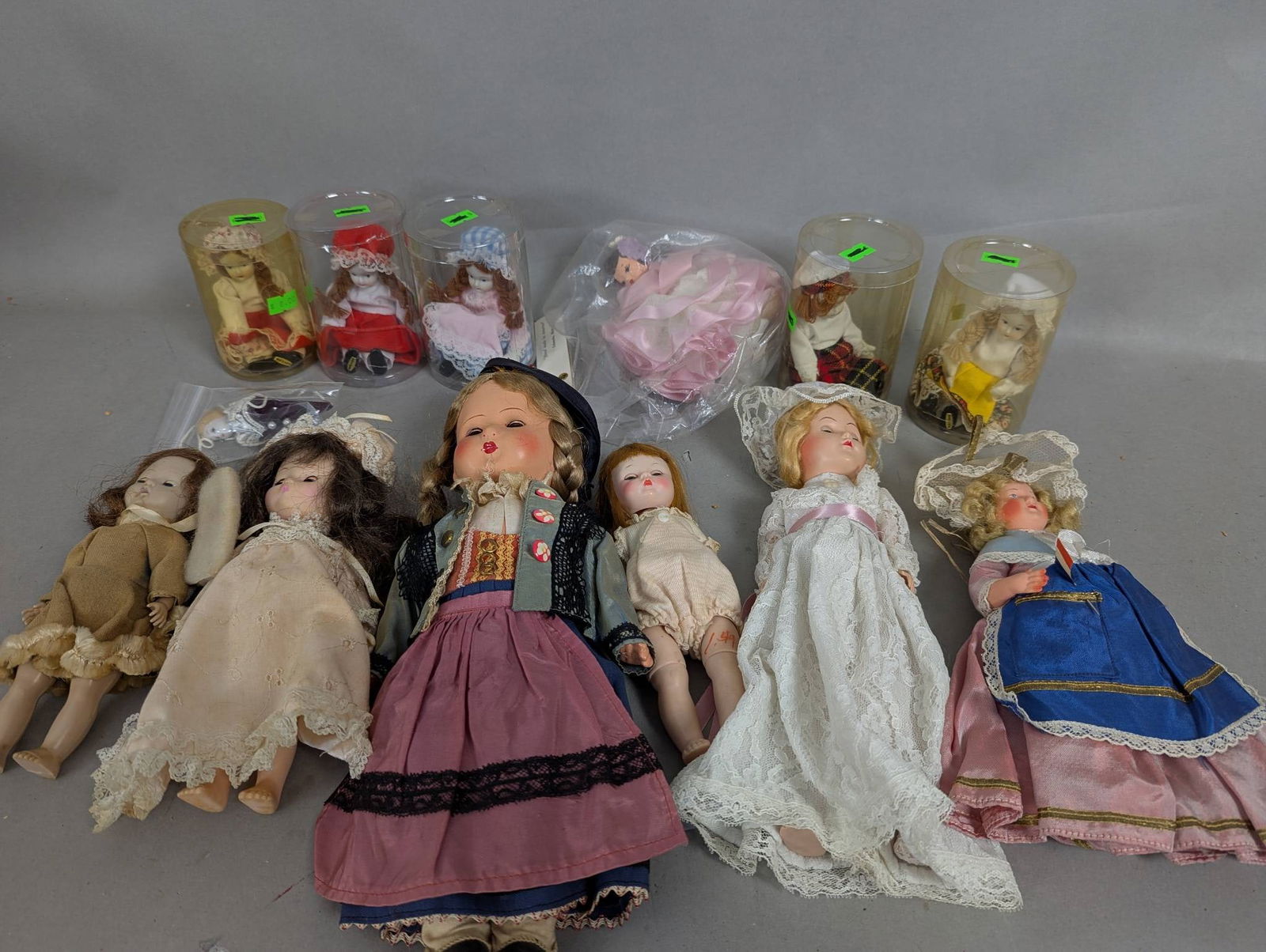 13 Assorted Vintage Dolls Including Hard Plastic and Bisque: 13 assorted vintage dolls ranging in height from 4 to 13 inches. The collection includes dolls made of hard plastic and bisque, dressed in various outfits, with some stored in plastic containers or pl