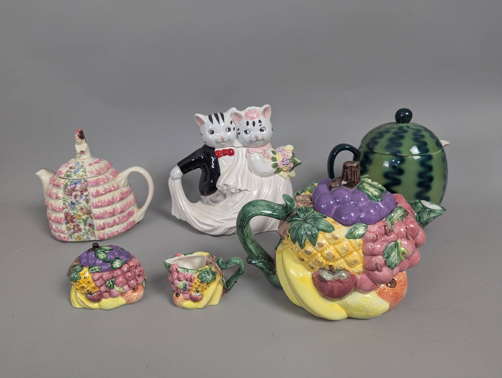 Teapots and Items Including Sadler, Skafford, and Dolomite: Four teapots, one cat-shaped pot, one fruit-themed dolomite teapot with a matching sugar and creamer set, and a watermelon-shaped Skafford teapot. The cat pot measures 9 inches high, 9 inches wide, an