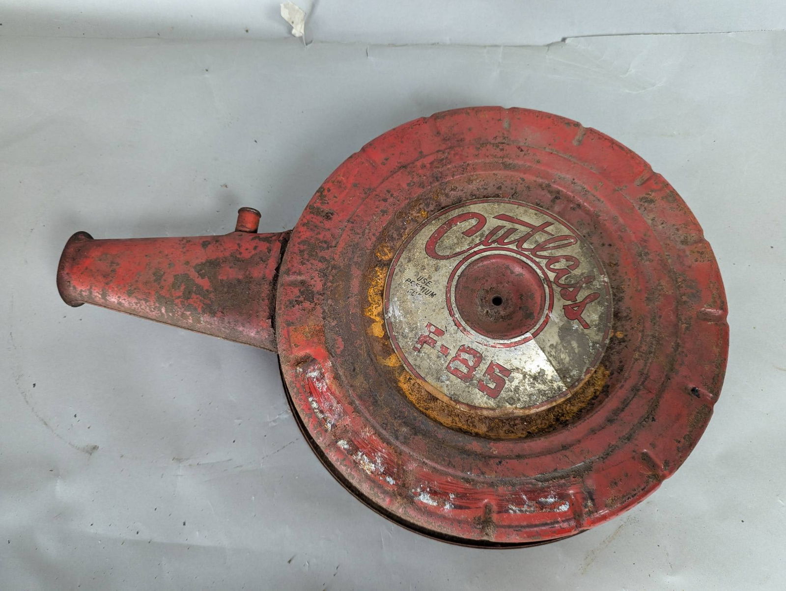 Red Oldsmobile Cutlass F85 Air Cleaner Assembly: Oldsmobile Cutlass F85 air cleaner assembly featuring a red painted exterior with visible use wear consistent with age. Displays the Cutlass and F85 logos on the lid. Made of metal with dimensions of