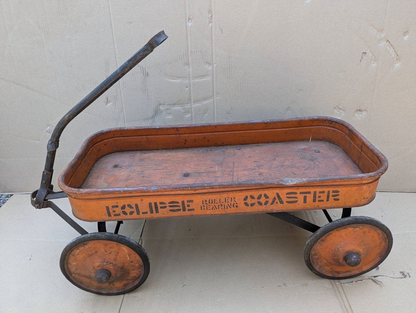 Eclipse Roller Bearing Coaster Wagon with Orange Finish: Eclipse Roller Bearing Coaster wagon constructed of metal with an orange finish. The wagon features four metal wheels and a movable handle. The lettering on the sides reads 'Eclipse Roller Bearing Coa