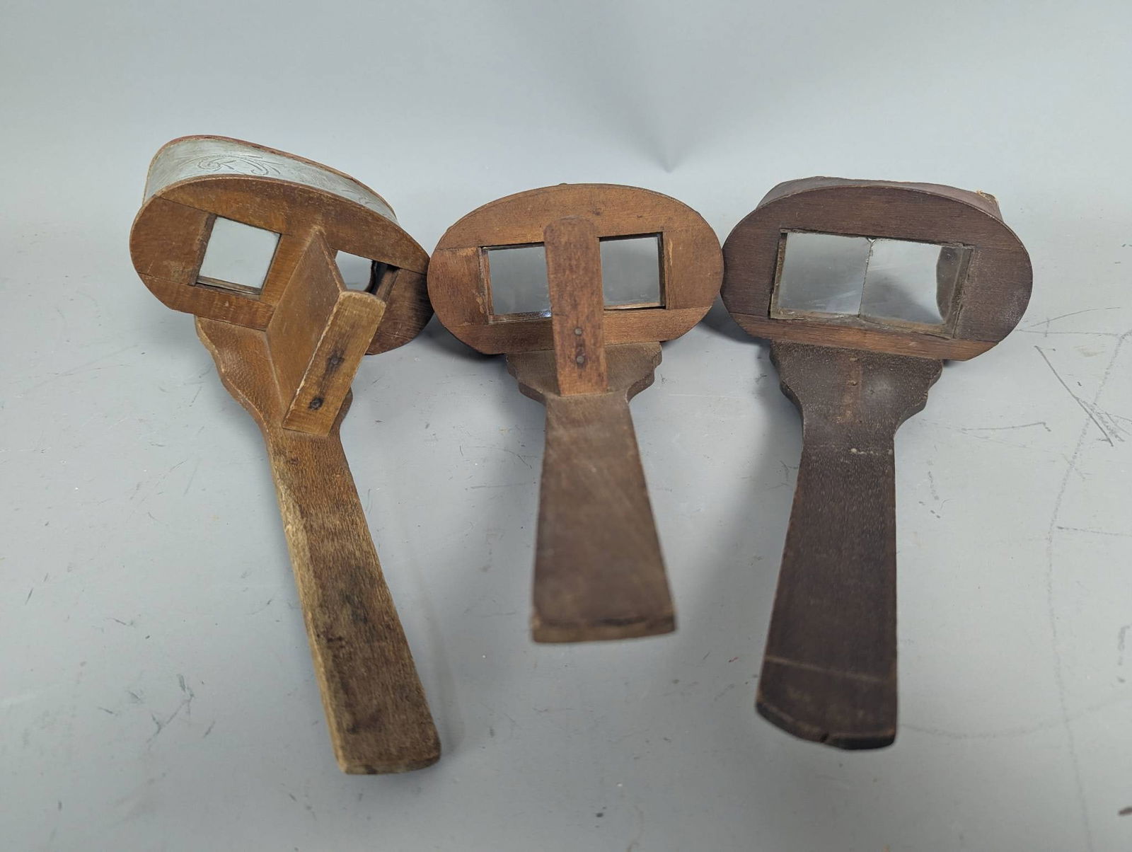 Three Antique Wooden Stereoscopes with Metal and Glass Components: Three antique stereoscopes crafted primarily from wood, featuring metal and glass elements. Each stereoscope is designed with two square viewing windows and includes a curved hood for comfortable use.
