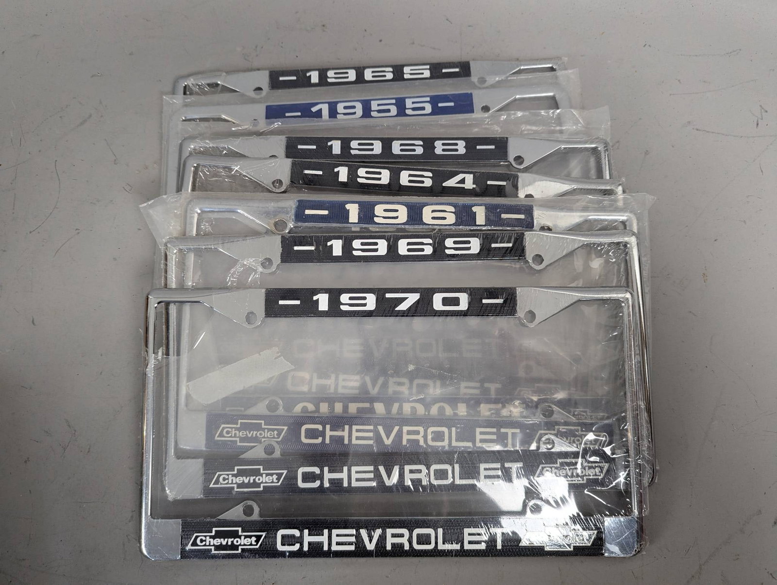 Chevrolet License Plate Frames Representing Various Years 1955-1970: Chevrolet license plate frames in chrome finish, each representing a different year: 1955, 1961, 1962, 1964, 1965, 1968, 1969, and 1970. The frames feature Chevrolet branding and year-specific designs