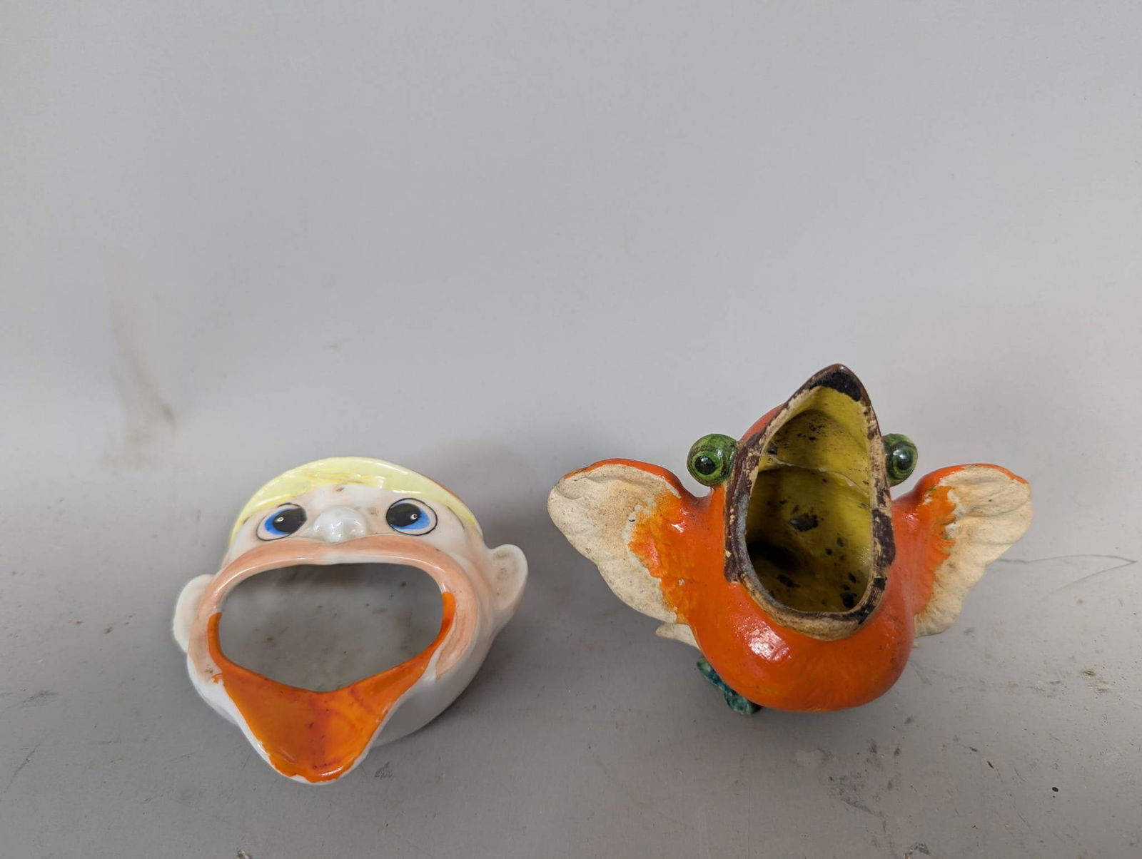 Vintage Ceramic Bird and Head Toothpick HoldersÂ Mid-20th Century: Two vintage ceramic toothpick holders likely from the mid-20th century, featuring a vibrant hand-painted bird and a realistic head design. The bird, painted in orange, green, and white hues, showcases