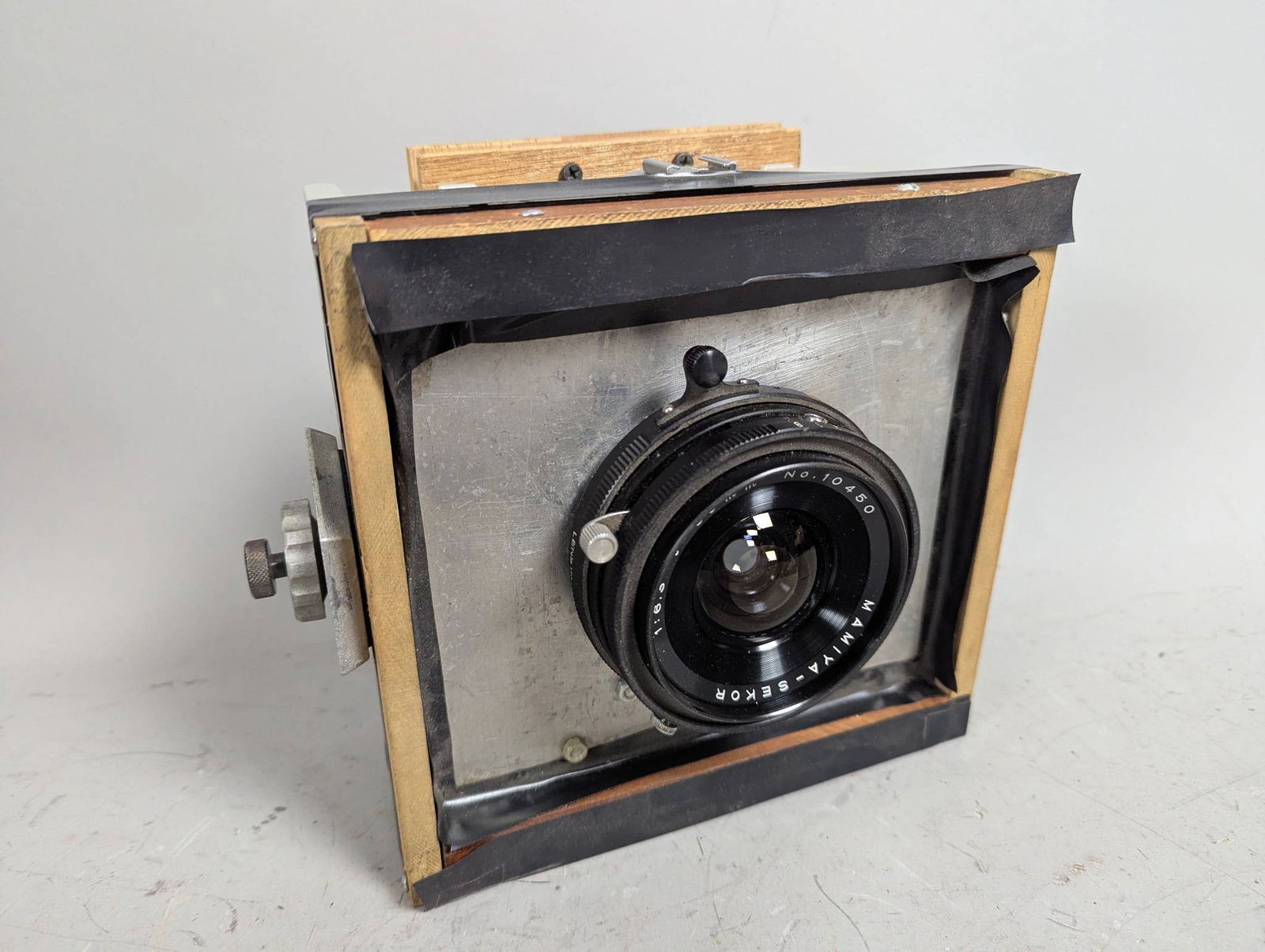 Mamiyakor Sekor 50mm Lens Mounted on Custom Camera Body: Custom camera body featuring a Mamiyakor Sekor 50mm f/6.3 lens with serial number 10450. The body is constructed with a combination of metal, wood, and hardware, reflecting a utilitarian design. Dimen