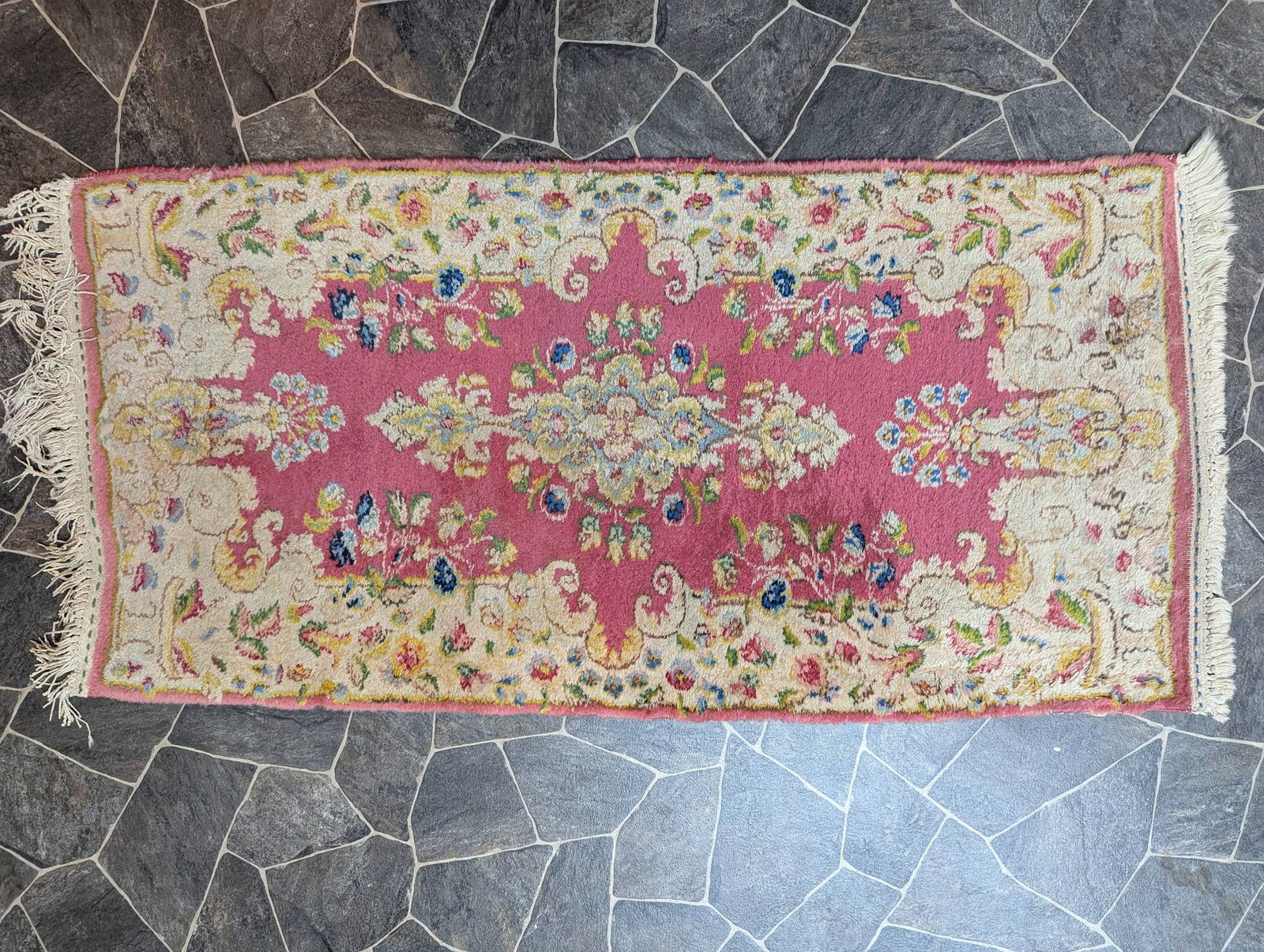 Pink Aubusson-Style Rug with Floral Medallion Design: Pink Aubusson-style rug featuring a central floral medallion design surrounded by intricate detailing of flowers and leaves. The rug has dimensions of 51 inches long by 25 inches wide. The border and 