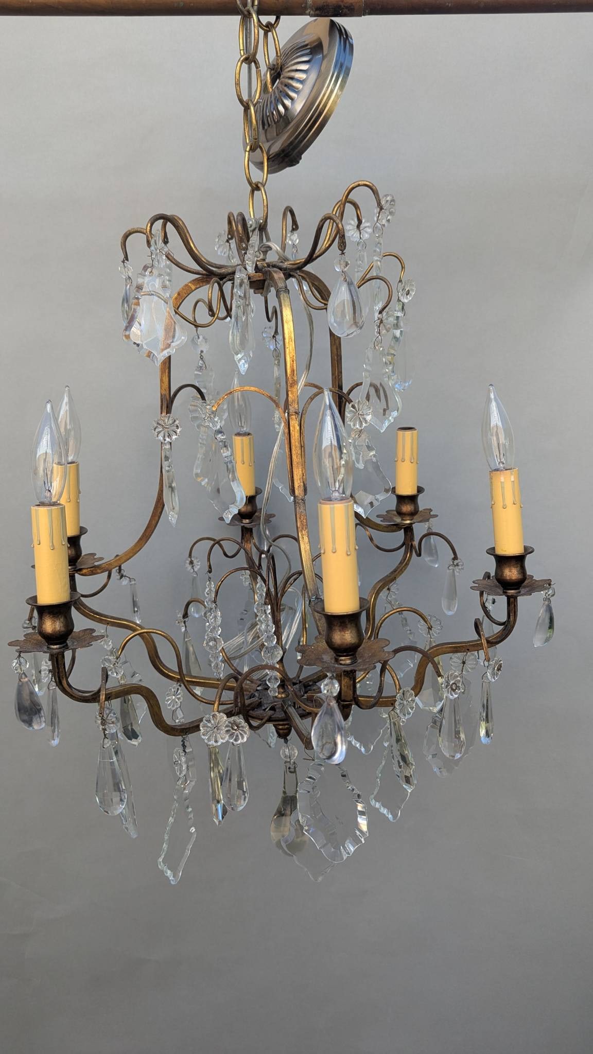 French Gilded Chandelier with Crystal Drops in Working Condition: Elegant French gilded chandelier featuring intricate crystal drops and an ornate metal frame. Includes multiple light sockets designed with candle-style holders. Measurements are 28 inches high, 15 in
