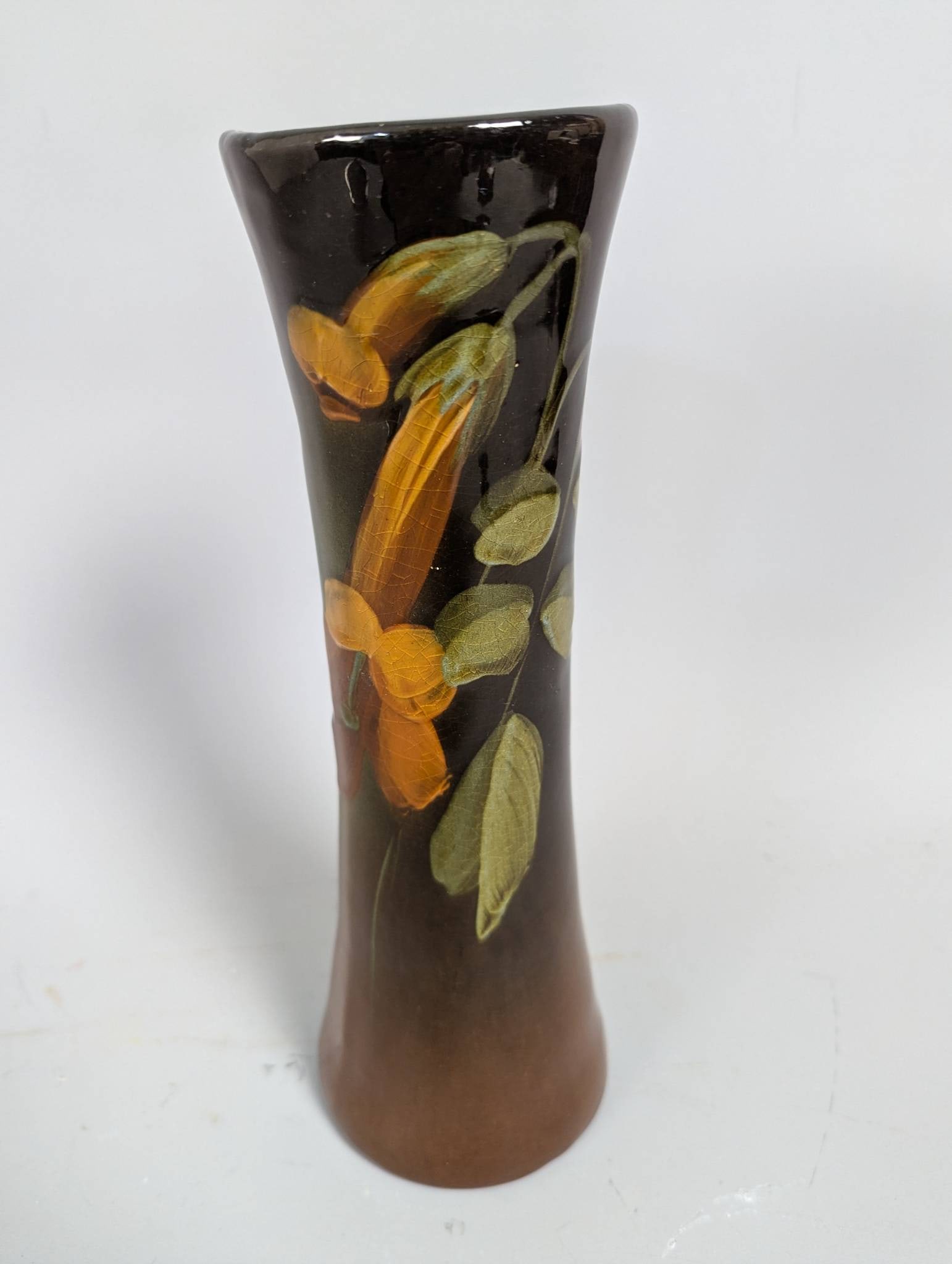 Rookwood Ceramic Vase with Hand-Painted Floral Decoration: Rookwood ceramic vase standing 10 1/2 inches high, 3 1/2 inches wide, and 3 1/2 inches deep. The piece features hand-painted floral decorations in hues of orange and green on a warm brown gradient gla