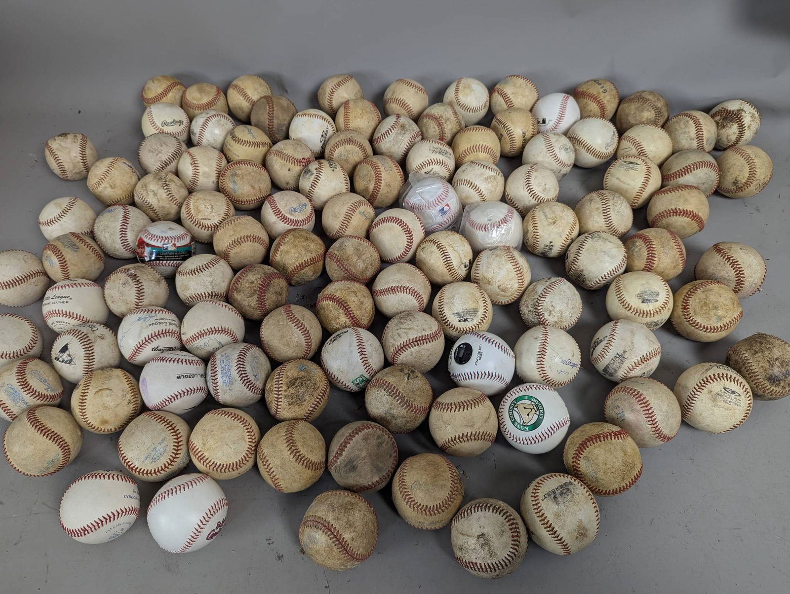 Baseballs Including Rawlings and Little League: 106 baseballs comprising various brands such as Rawlings, MacGregor, and Little League. Some balls show signs of wear and field use, and a few appear to have markings or signatures. The grouping inclu