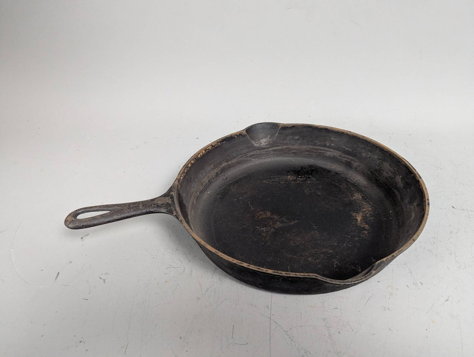 Cast Iron Skillet with Pour Spouts and Handle: A cast iron skillet featuring integrated pour spouts on either side and a sturdy handle with a hanging hole. Measures approximately 16 inches high, 12 inches wide, and 2 inches deep, with an 11-inch d