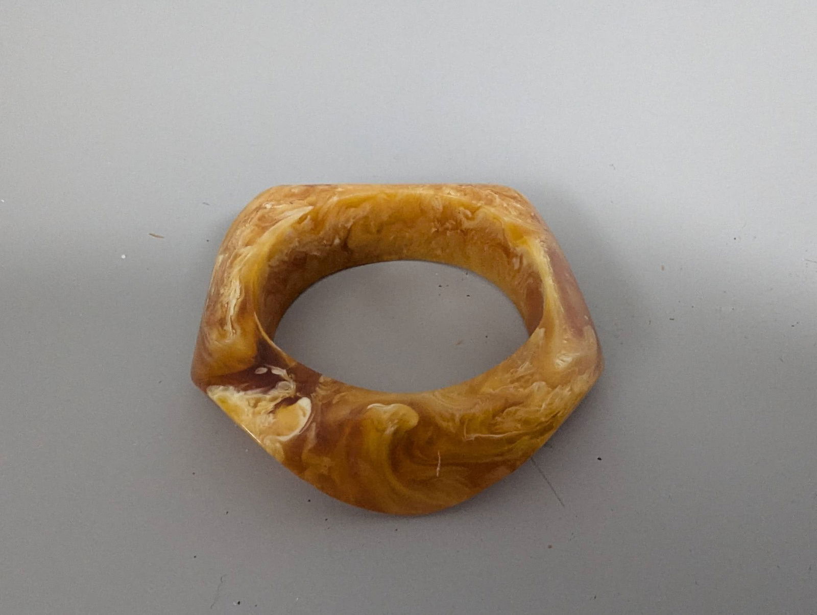 Vintage Yellow Marbled Lucite Bangle Bracelet with Asymmetrical Shape: A vintage yellow marbled lucite bangle bracelet featuring a sculptural asymmetrical shape. The bracelet displays a striking marbled pattern that gives it a unique aesthetic. The dimensions of the brac