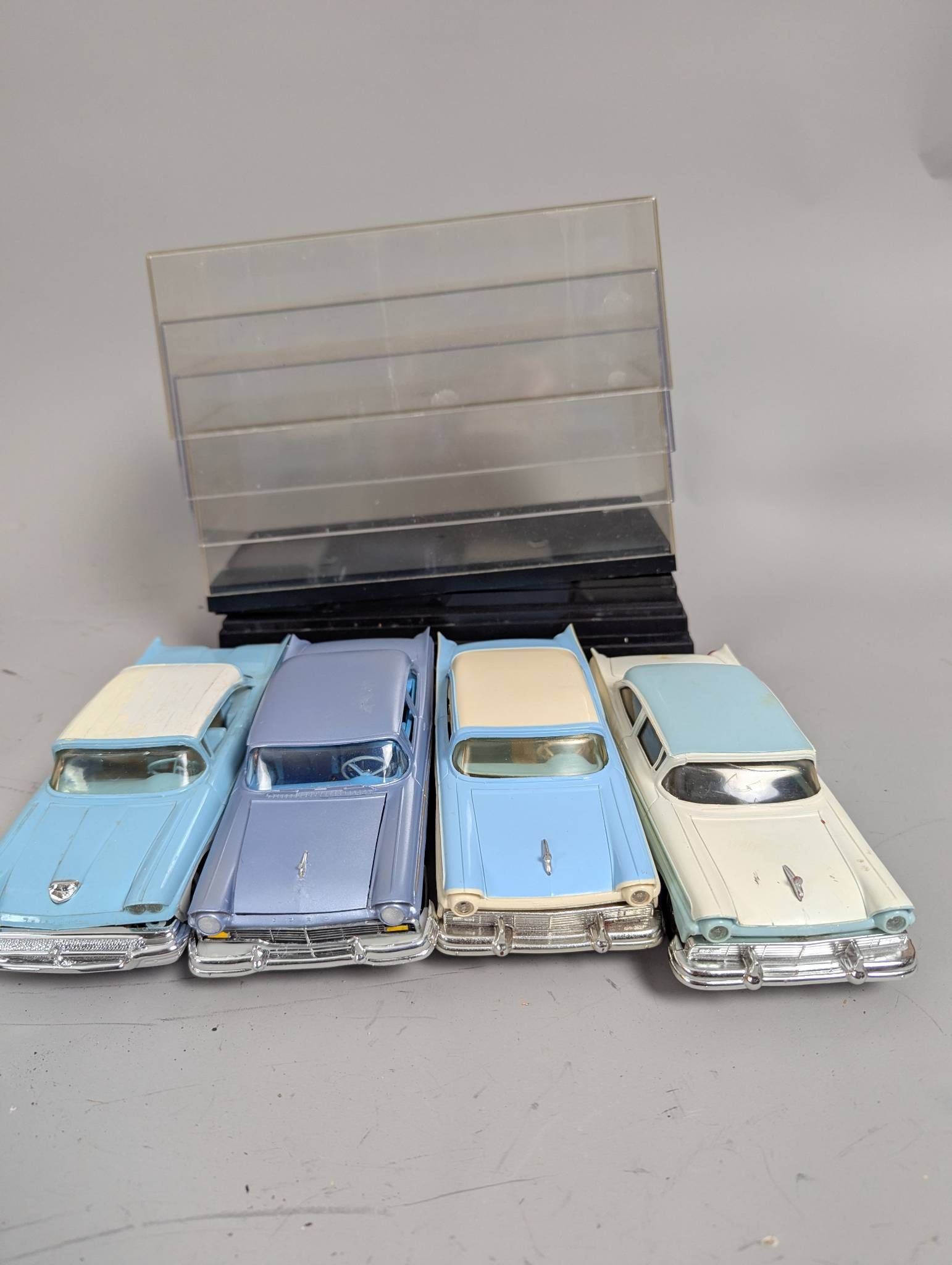 1950s Plastic Promotional Model Cars in Display Cases: Four 1950s promotional model cars, housed in plastic display cases. Each car measures approximately 8 inches high, 5 inches wide, and 3 inches deep. The models are highly detail-oriented, representing