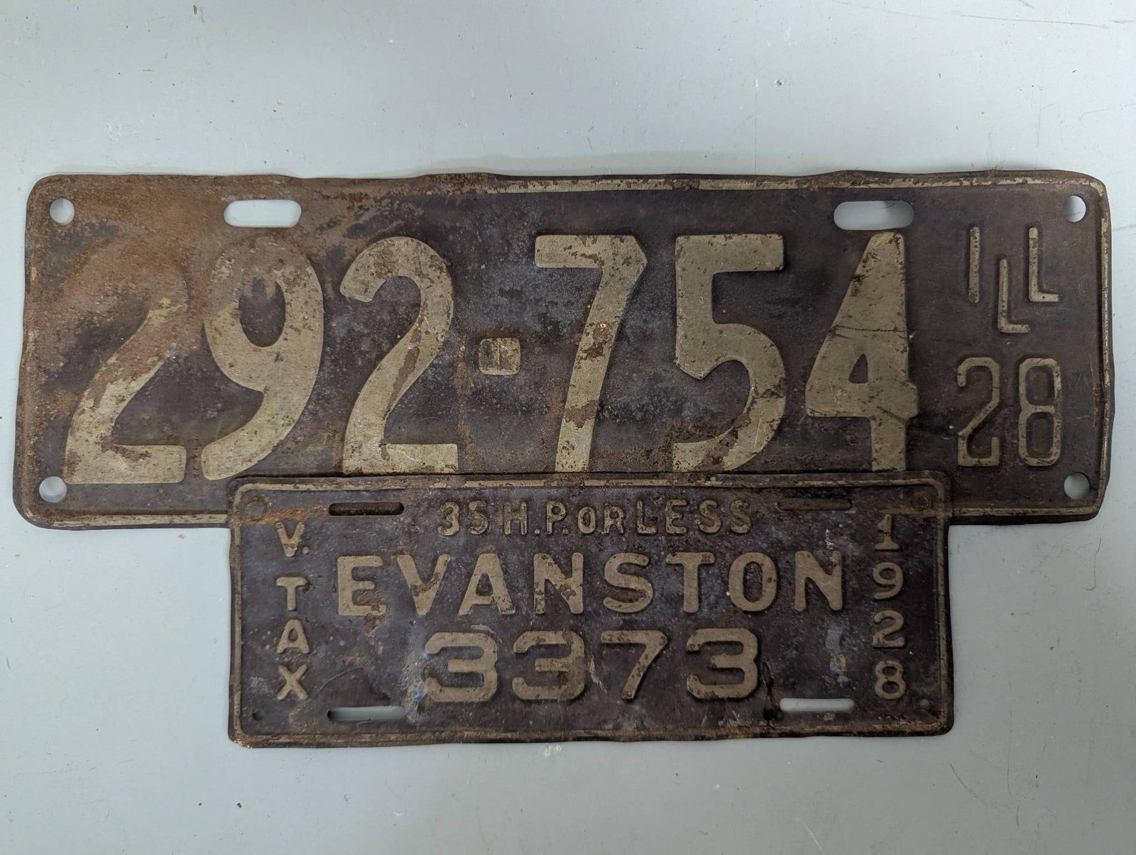 Early 20th Century Illinois and Evanston License Plates 1928: Early 20th-century license plates, including one from Illinois marked with the number 292-754 and dated '28, and another from Evanston marked 3373 with additional details such as '35 H. Powerless'. Bo