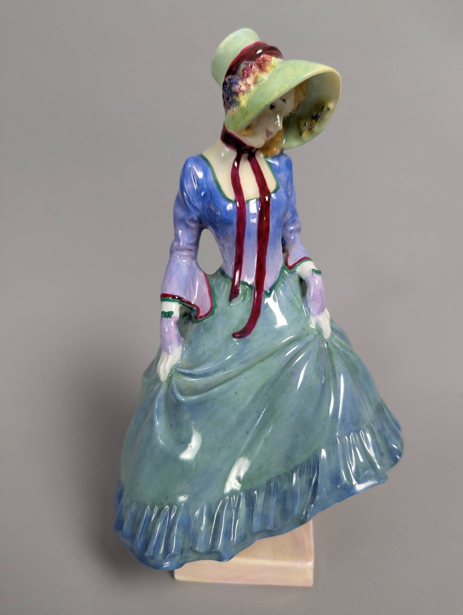Royal Doulton HN1362 Pantalettes Figurine in Hand-Painted Glaze: Royal Doulton HN1362 figurine titled Pantalettes, designed in a charming pose with hand-painted details. The piece depicts a woman in period attire, featuring a blue top and flowing green skirt along 