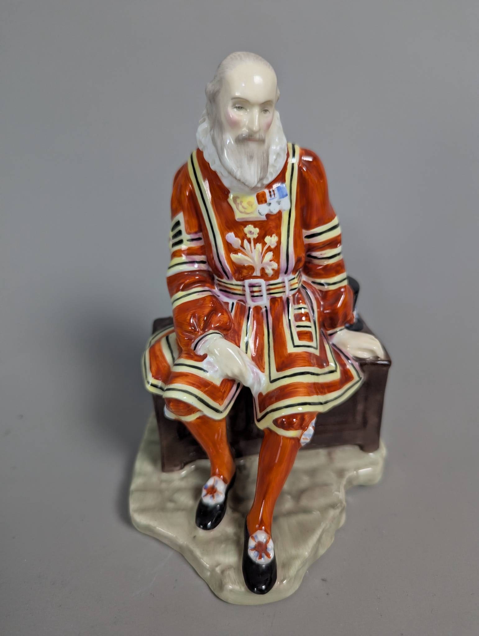 Royal Doulton HN 2122 A Yeoman of the Guard: A ceramic figurine by Royal Doulton titled A Yeoman of the Guard, model number HN 2122. Standing 6 inches high, this piece depicts a Yeoman of the Guard in detailed traditional attire, seated on a ben