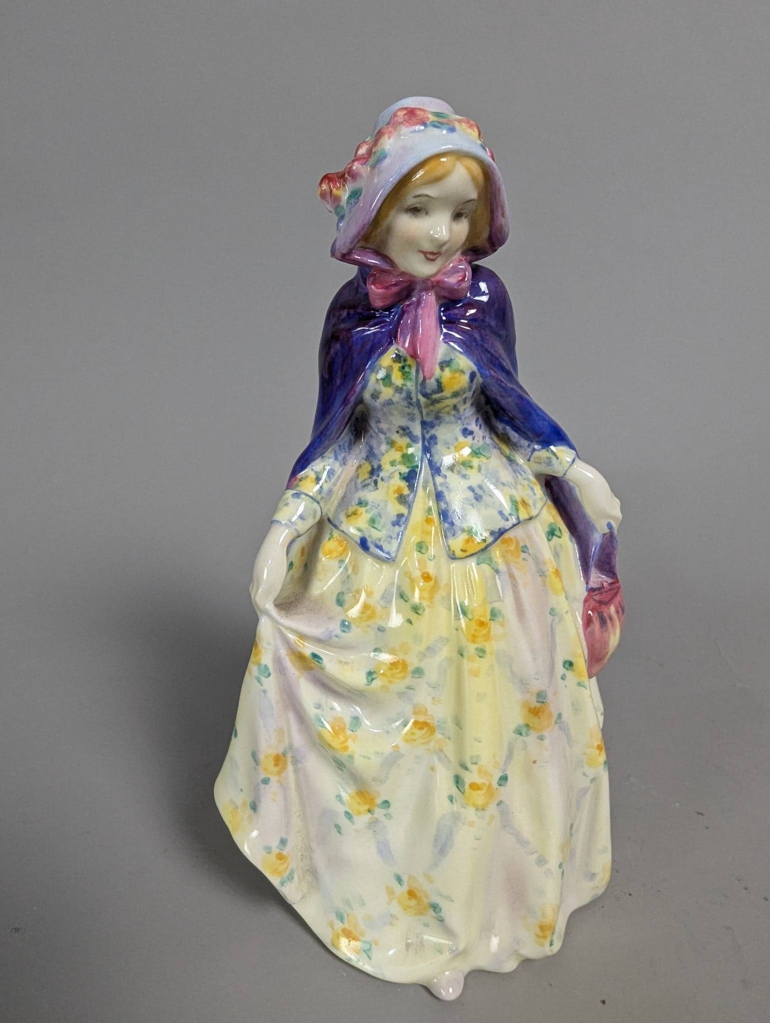 Royal Doulton Jennifer HN 1484 Figurine in Floral Dress and Purple Cape: Royal Doulton figurine titled Jennifer, model HN 1484. The ceramic piece stands 7 inches high and features a woman in a flowing floral dress with a purple cape and bonnet adorned with flowers. The bas