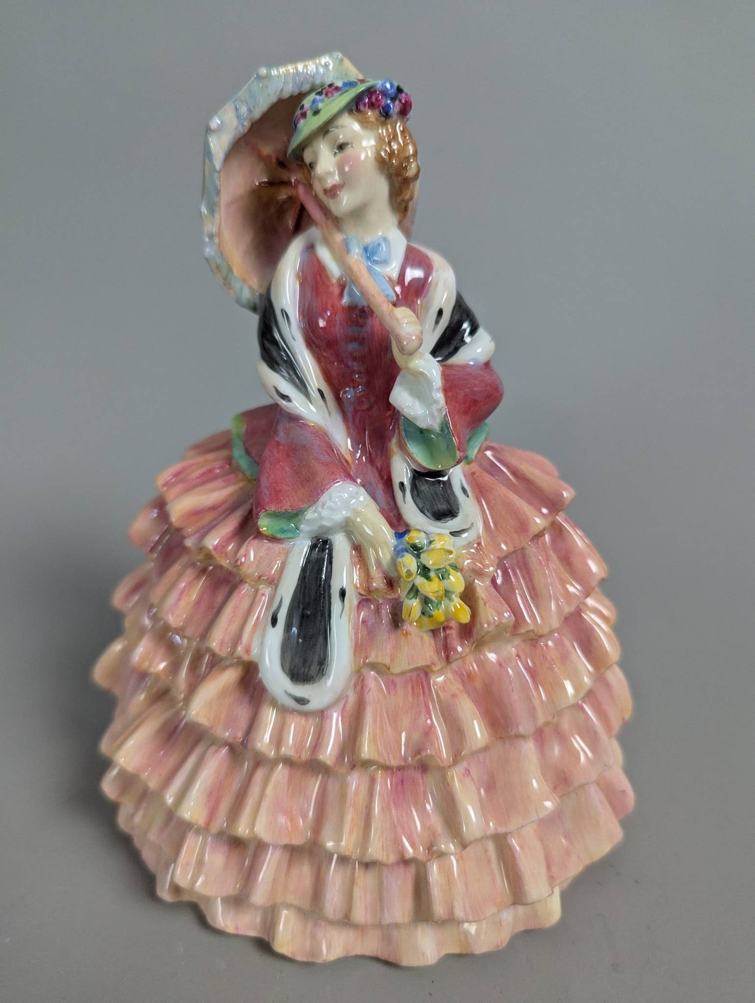 Royal Doulton HN 1940 Toinette Porcelain Figurine: Royal Doulton porcelain figurine titled Toinette, model HN 1940. The piece features intricate detailing of a woman dressed in an elegant layered gown, holding a parasol and flowers. Marked with the Ro
