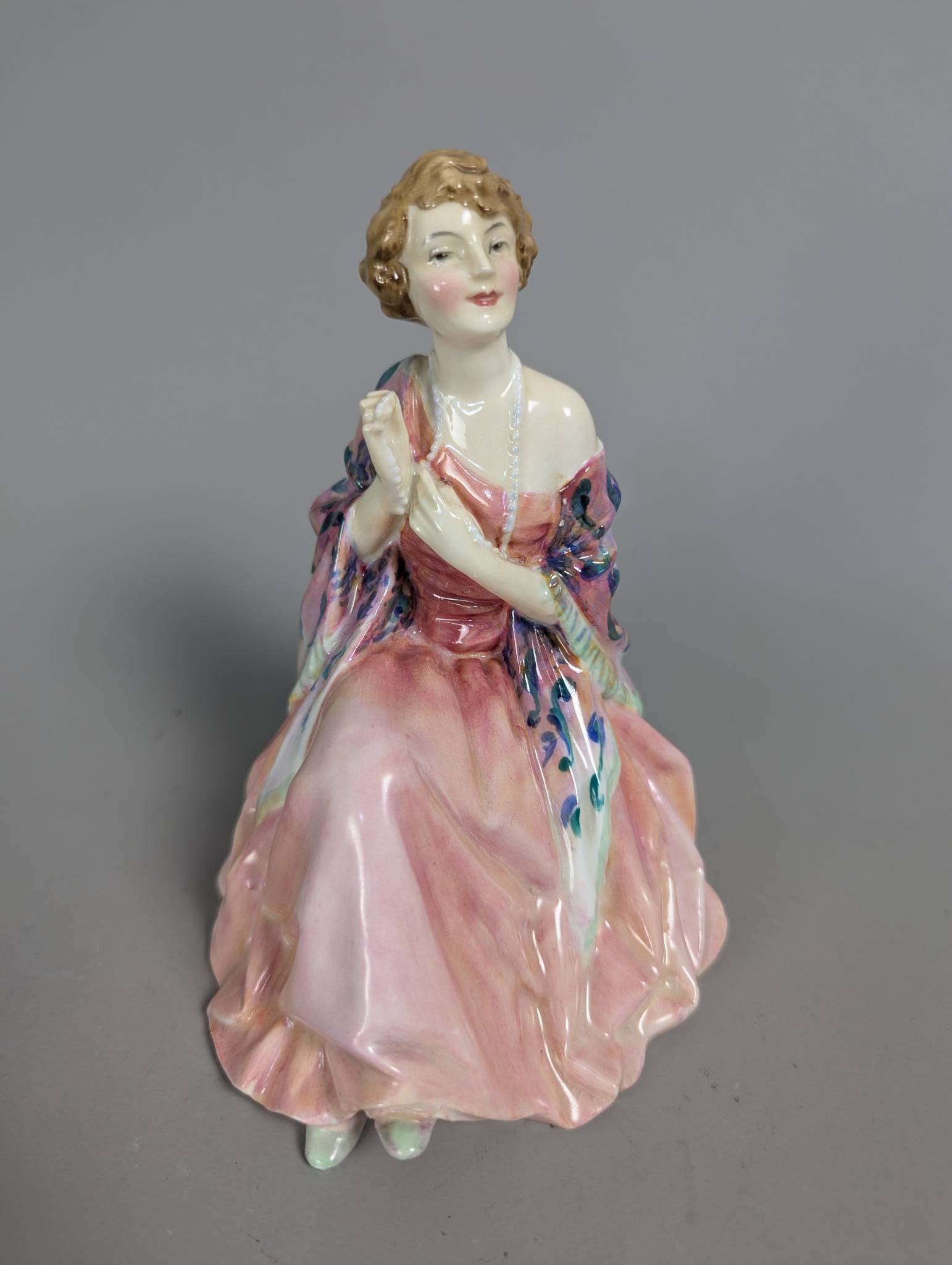 Royal Doulton Hn 1664 Aileen Porcelain Figurine: Royal Doulton porcelain figurine titled Aileen, model number HN 1664. Measuring 6 1/2 inches high, the figure depicts a seated woman in a flowing pink dress with a decorative shawl featuring blue and
