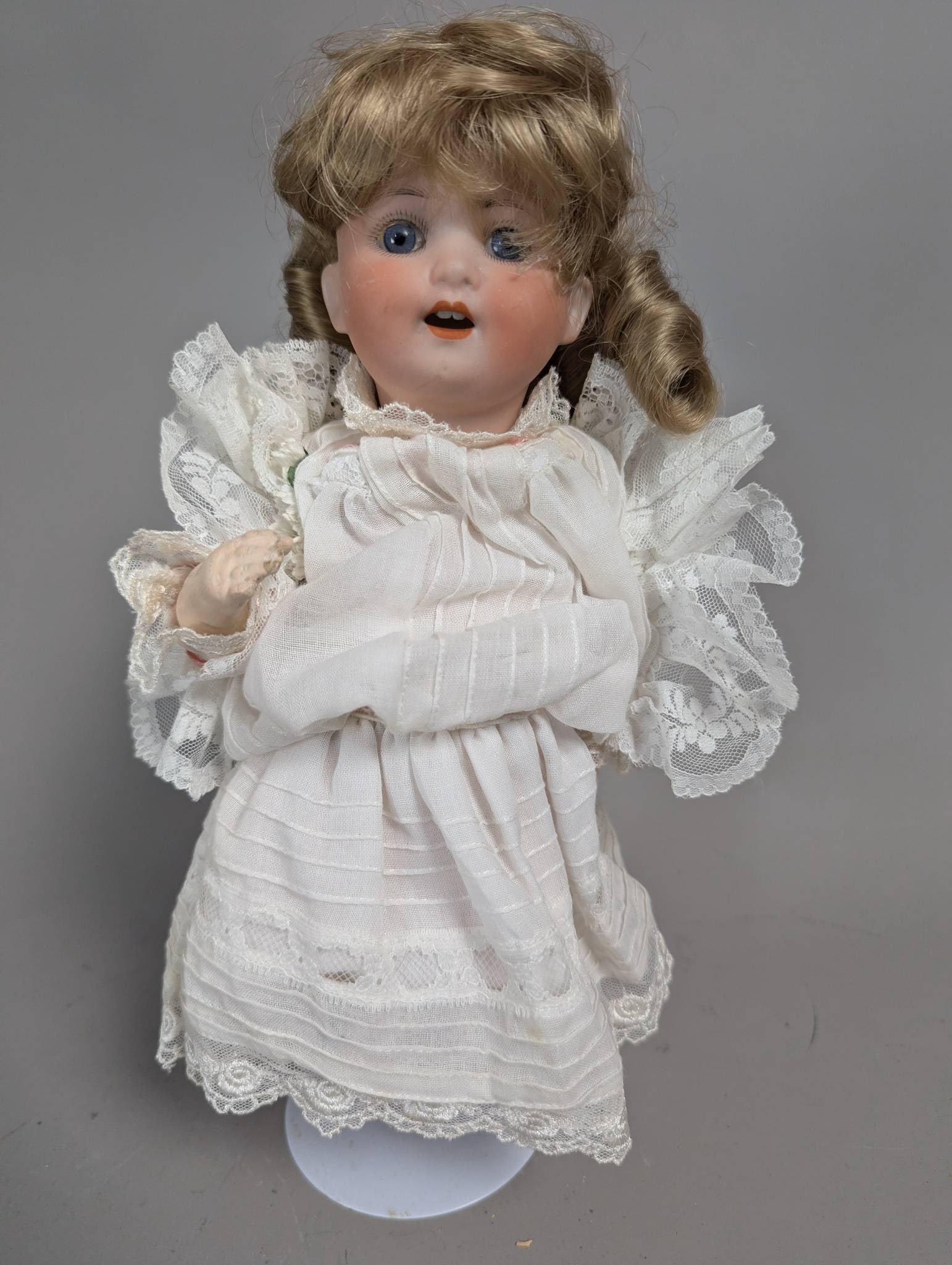 Heubach Koppelsdorff Bisque Head Doll with Blonde Hair and Lace Dress: A Heubach Koppelsdorff bisque head doll measuring 12 inches high, featuring blue glass eyes, blonde hair styled in curls, and an embroidered white lace dress. The doll's head is marked 'Heubach Koppel
