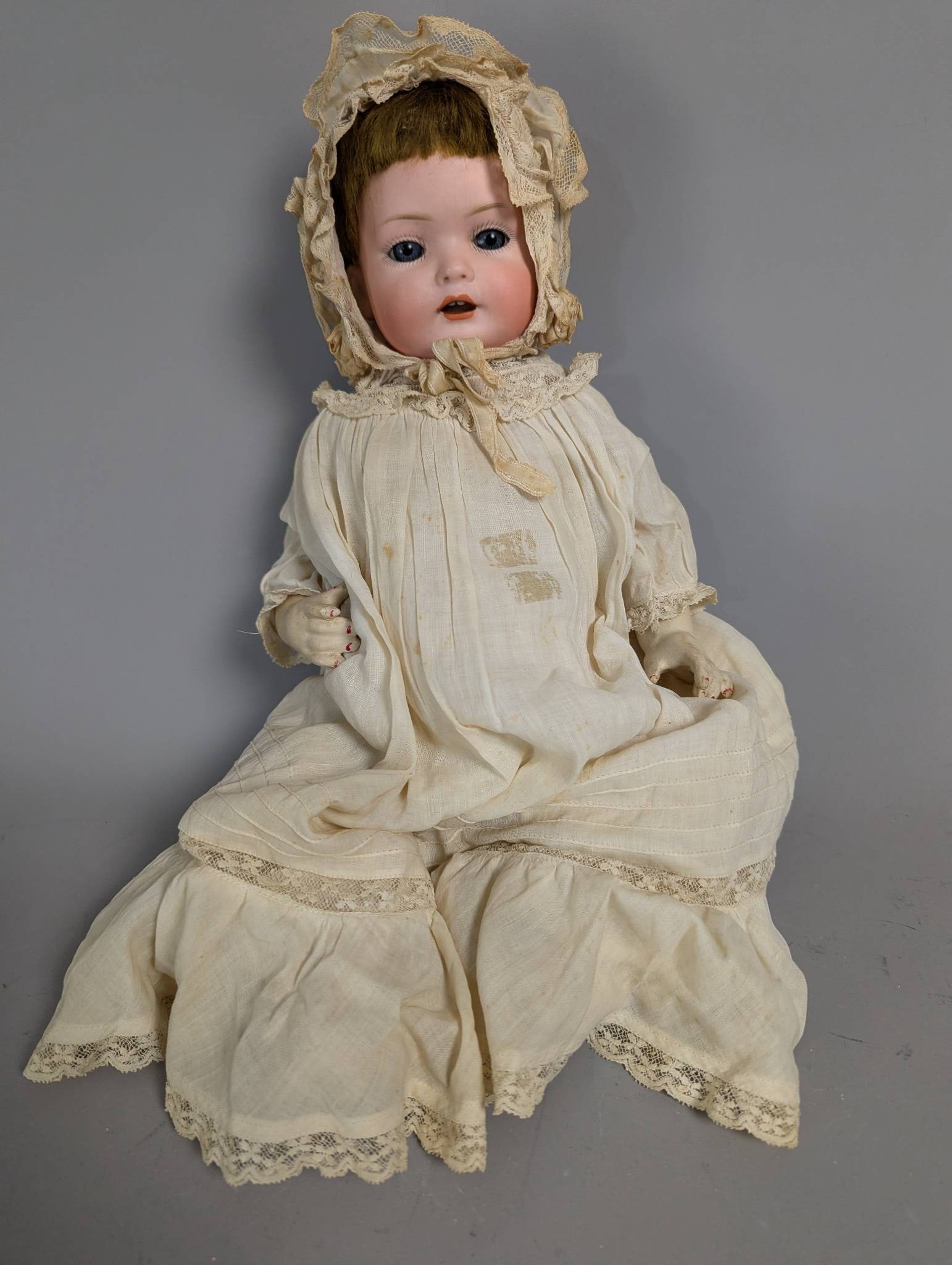 Bergmann and Co German Bisque Head Baby Doll in Lace Dress: German bisque head baby doll marked Bergmann and Co, measuring 15 inches high. Features include sleep eyes, open mouth with teeth, and composition body. The doll is clothed in a cream lace dress with