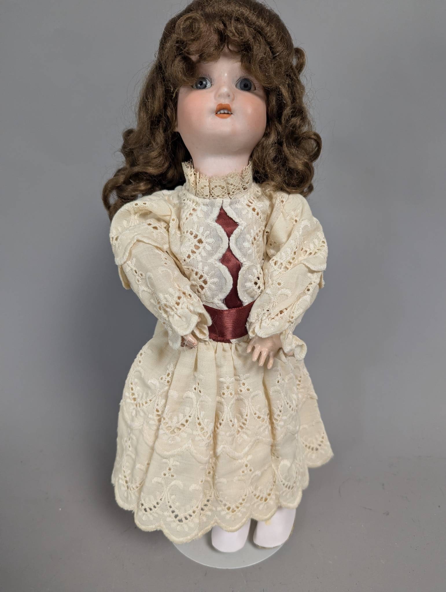 Simon and Halbig Bisque Head Doll with Lace Dress and Brown Hair: Simon and Halbig 15-inch bisque head doll featuring brown curly hair, blue glass eyes, and an open mouth with teeth. The doll wears a vintage-inspired lace dress with red accents and includes matching