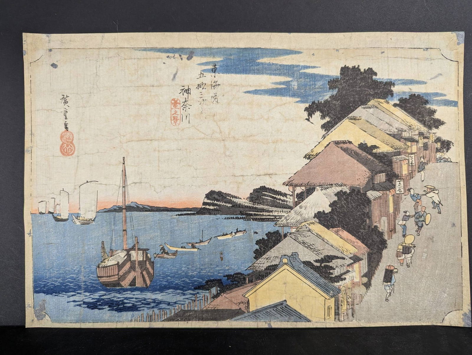 Japanese Woodblock Print Depicting Kanagawa by Ando Hiroshige: Japanese woodblock print by Ando Hiroshige (1797-1858), titled Kanagawa, part of the Hoeido Tokaido series, created in 1833. The print depicts a coastal scene with a bustling village, a harbor featuri