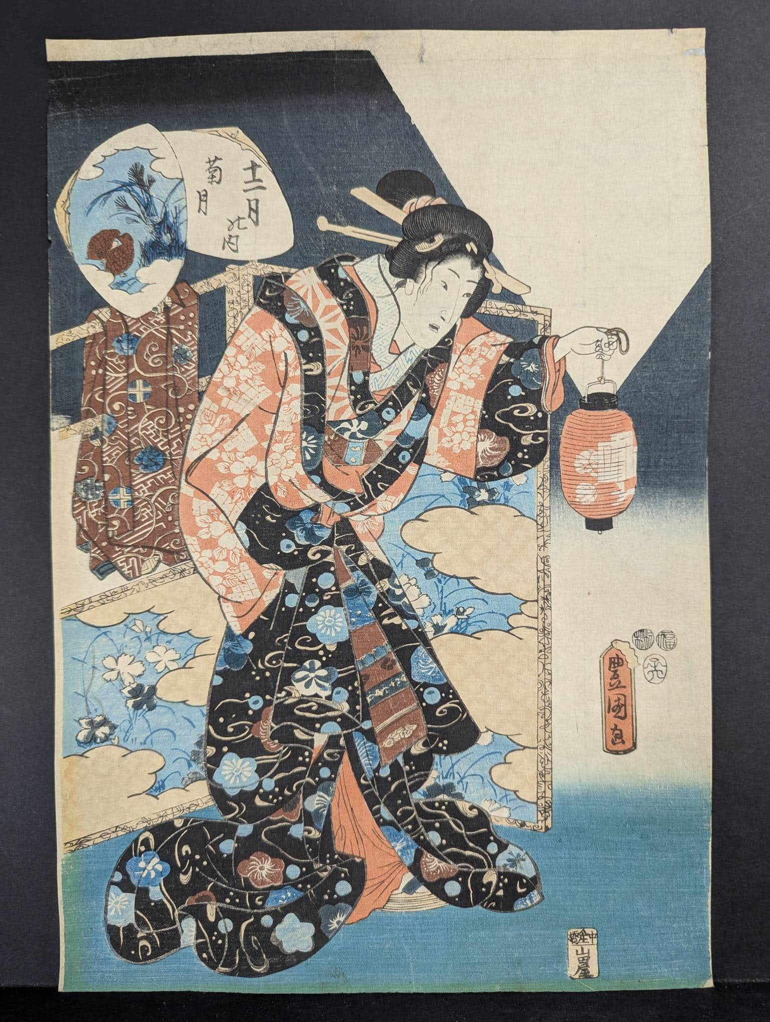 Japanese Woodblock Print Depicting a Woman with Lantern by Utagawa Toyokuni III: Japanese woodblock print attributed to Utagawa Toyokuni III (1786-1875), depicting a woman holding a lantern with intricate patterns on her kimono. The print features elements of blue clouds, floral m