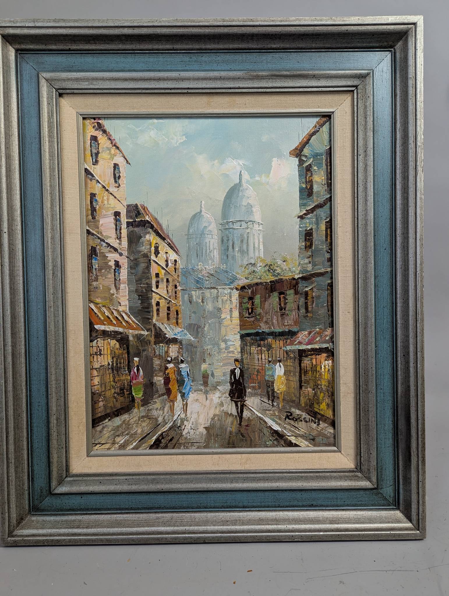 Impressionist Oil on Canvas Painting by Rossini Depicting Street Scene: Impressionist oil on canvas painting by Rossini. The artwork portrays a quaint street scene with figures walking along a cobbled road, with detailed architecture and domed structures in the background
