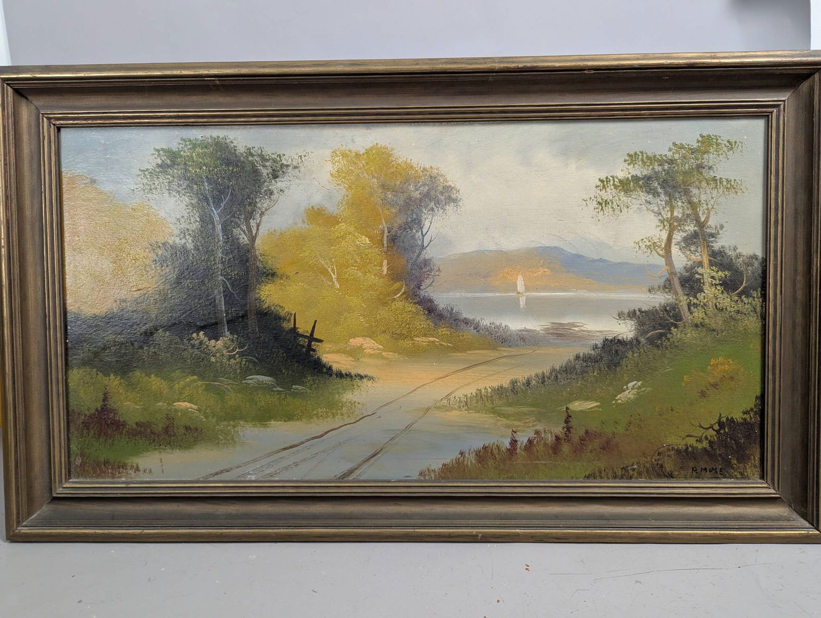 Oil Painting on Board Signed Lower Right R Mose Depicting a Landscape Scene: Oil on board painting signed lower right by R Mose, featuring a serene landscape with a dirt path leading toward a body of water, bordered by trees and vibrant foliage. The painting measures 29 1/2 in
