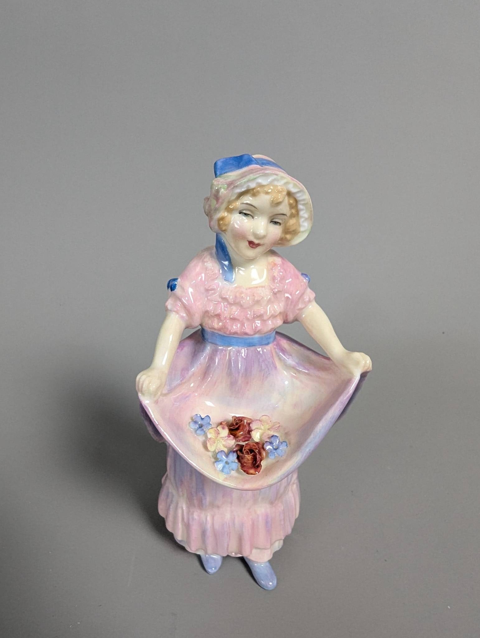 Royal Doulton Lucy Ann Figurine in Pastel Tones: Royal Doulton Lucy Ann figurine crafted in fine bone china. Featuring a young girl dressed in a pastel pink and blue outfit holding the hem of her dress decorated with floral detailing. The figurine