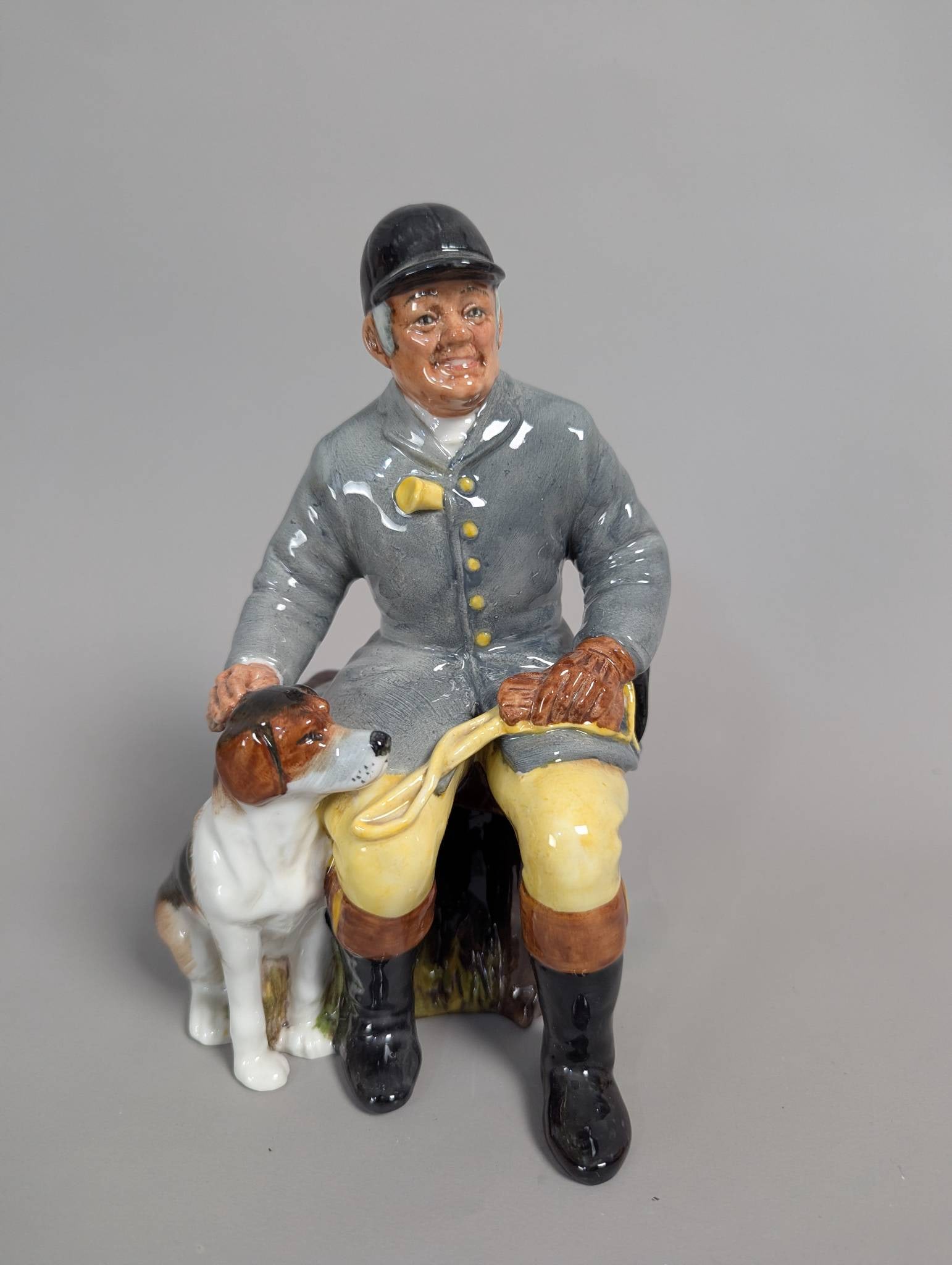 Royal Doulton HN2492 The Huntsman Figurine: Royal Doulton porcelain figurine titled The Huntsman, model number HN2492. The piece features a seated huntsman in traditional attire with a foxhound by his side and is hand-painted with intricate det