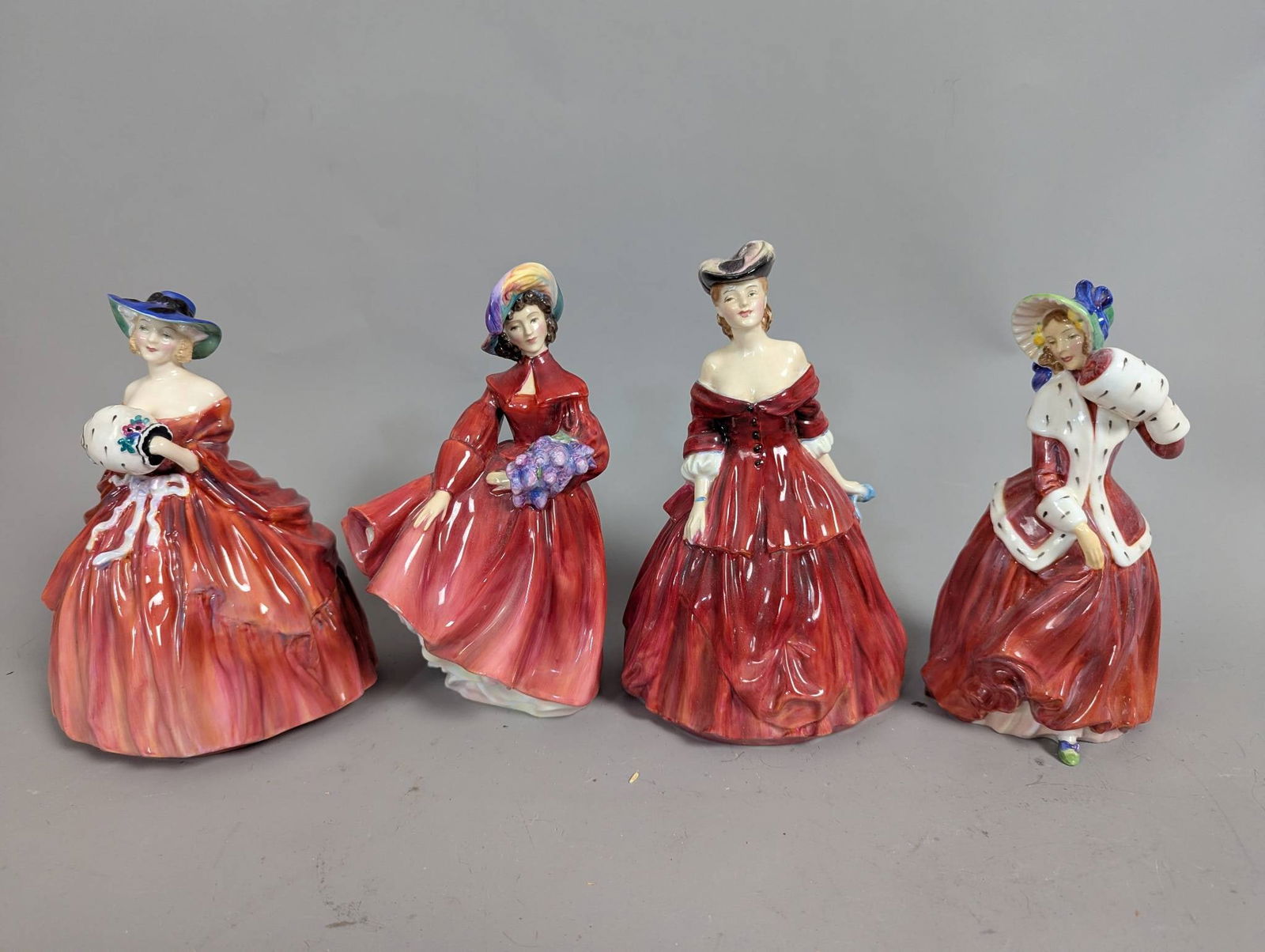 Four Royal Doulton Figurines in Red Hand-Painted Dresses: Four Royal Doulton porcelain figurines, each hand-painted with detailed designs. The set includes Genevieve (HN 1963), Lilac Time (HN 2137), Vivienne (HN 2073), and Christmas Morn (HN 1992). The figur