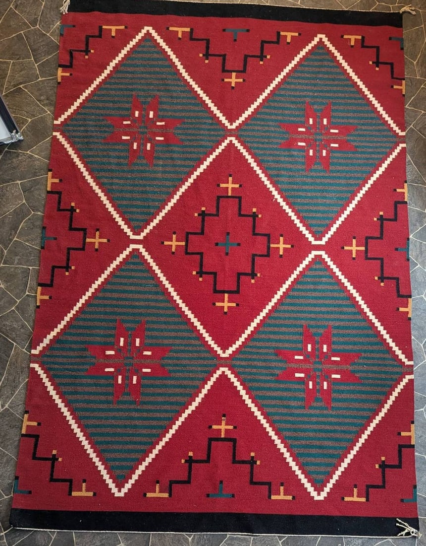 Navajo Wool Rug Featuring Geometric Patterns C1980s: A Navajo wool rug showcasing a striking geometric design in predominantly red, green, and cream tones. The rug features diamond and cross motifs accented by smaller linear patterns. Crafted in the 198