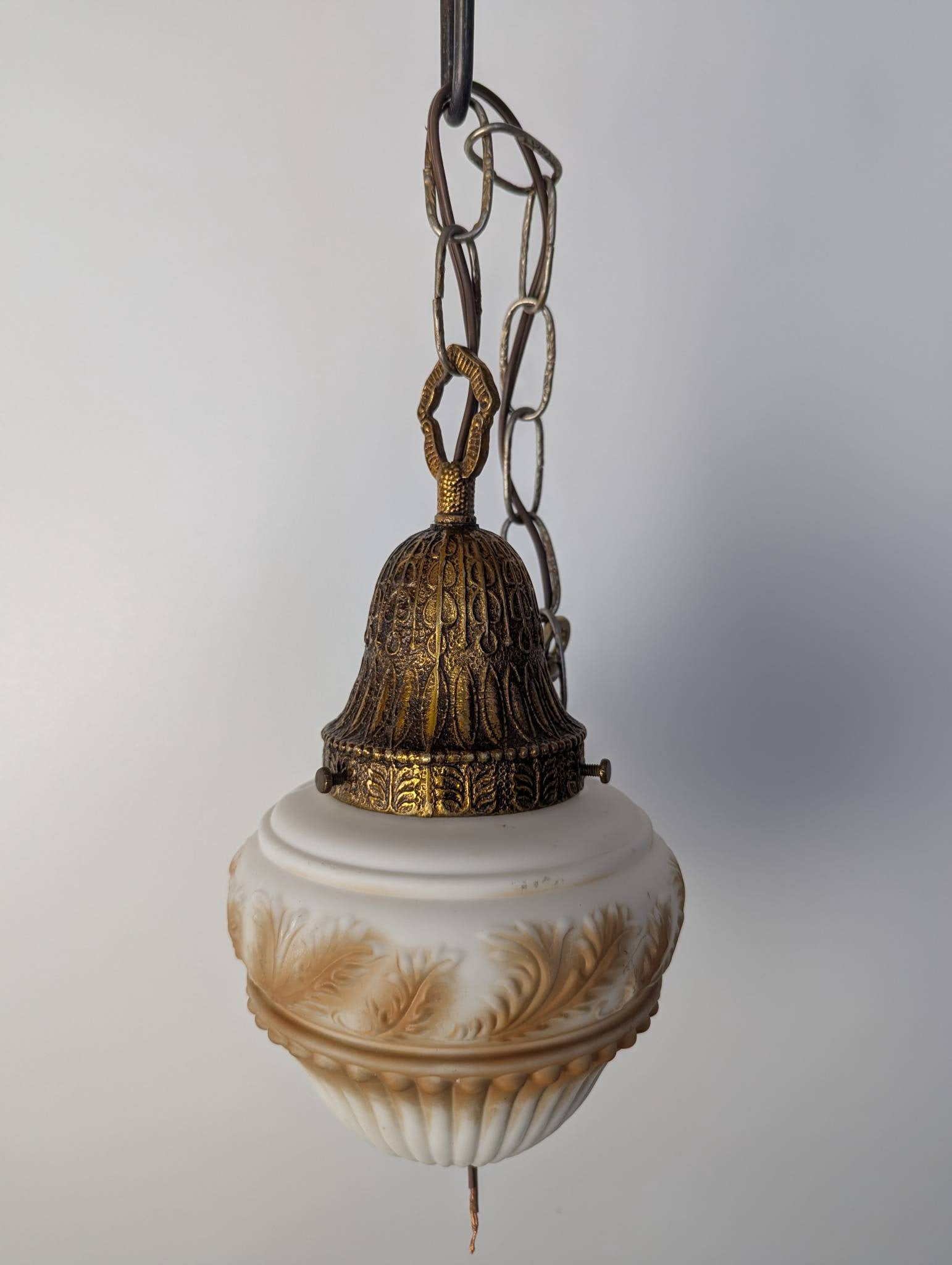 Art Nouveau or Hollywood Regency Pendant Light with Leaf Pattern Shade: Vintage pendant light featuring a brass or copper-finished fitter and a milk glass shade with an ornate leaf pattern. The shade measures 12 inches high and 7 inches in diameter. The light has been rew