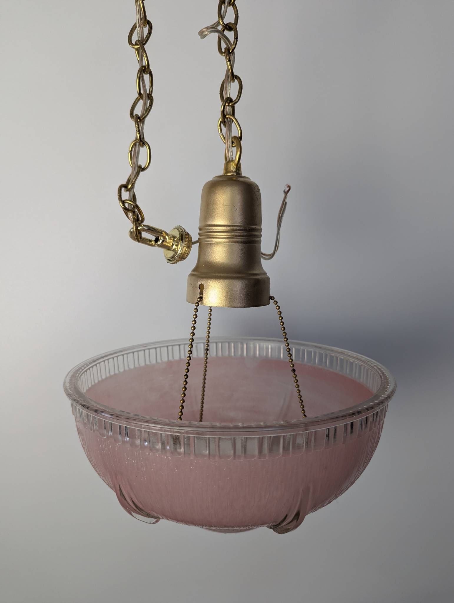 Vintage Art Deco Style Brass and Pink Glass Bowl Pendant Light Fixture: Vintage Art Deco-style pendant light fixture featuring a ribbed or fluted pink glass bowl suspended by three chains from a brass canopy. The pink glass bowl is accented with clear edges, creating a st