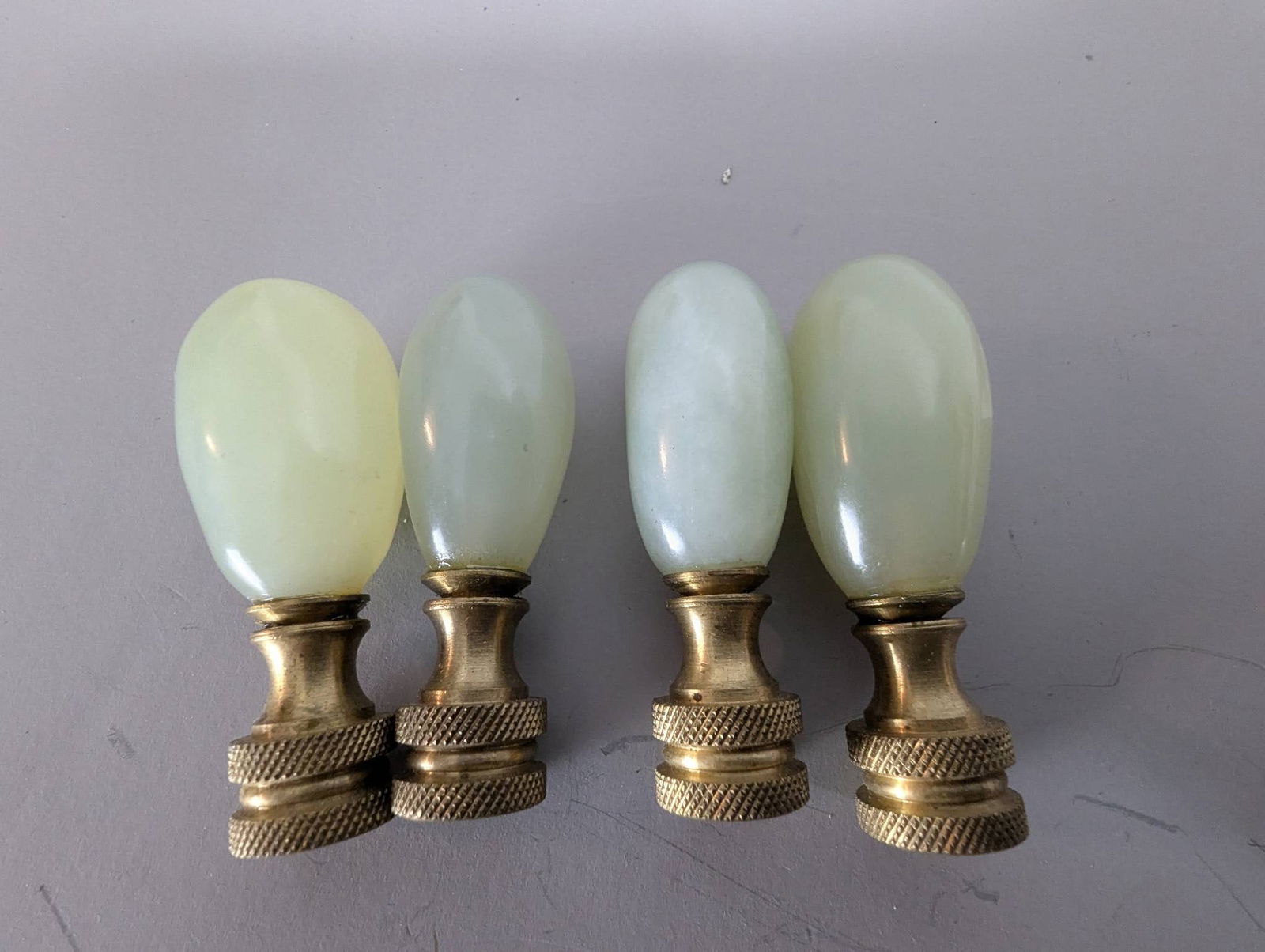 4 Vintage Jadeite Lamp Finials with Brass Bases: 4 vintage lamp finials crafted from jadeite or jade-like material, featuring brass bases. Each finial measures approximately 2 inches high by 3/4 inch wide and deep. The smooth green-toned surfaces