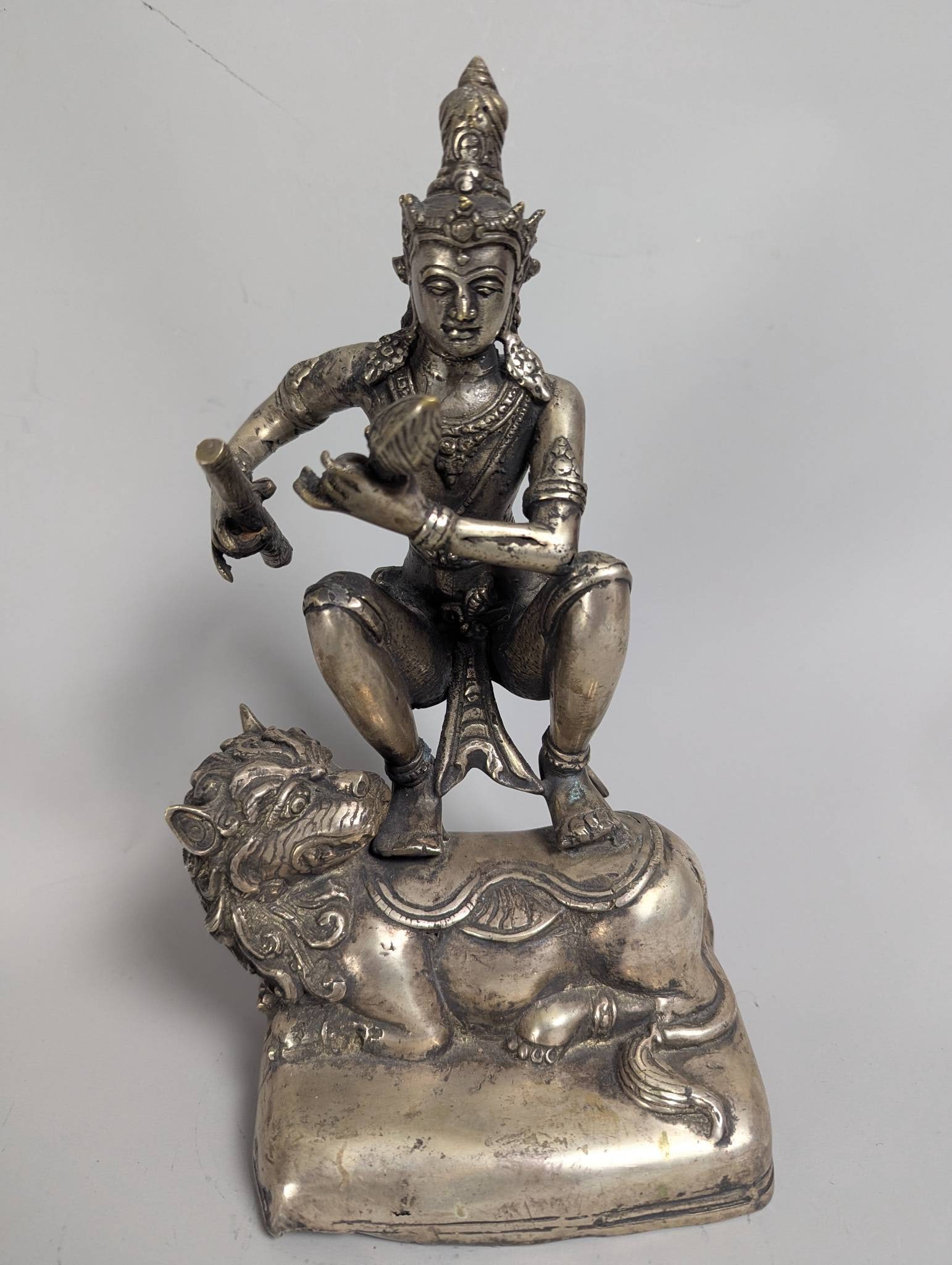 Achala Tibetan Buddhist Deity Statue on Snow Lion with Flaming Sword: A statue depicting the Tibetan Buddhist deity Achala, or Bagh Bhairava, standing in a dynamic pratyalidhasana posture with his right leg bent and left leg straight. The deity is mounted atop a